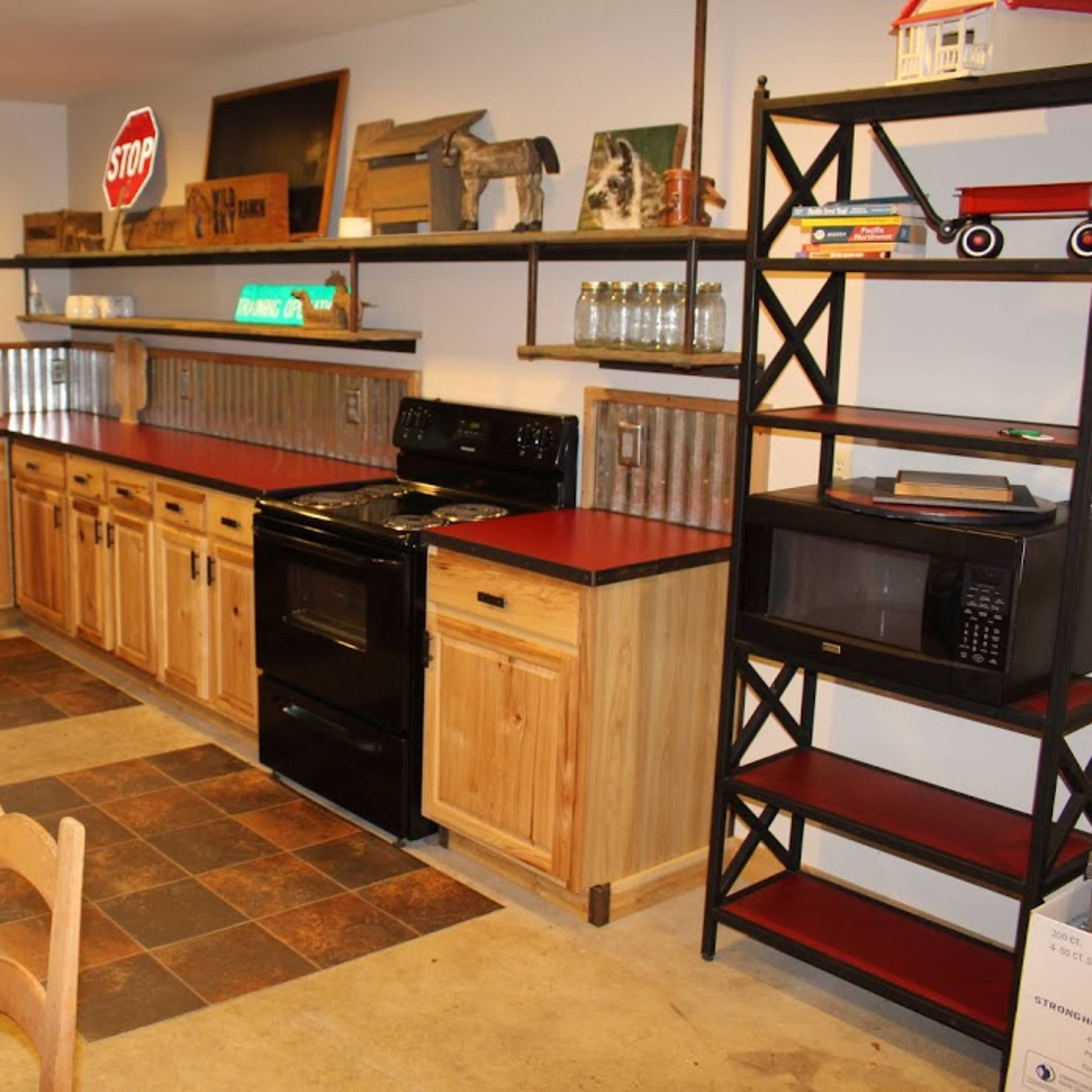 A kitchen with wooden cabinets, a black stove, a microwave, and open shelving, featuring a tiled floor and a small table with chairs.