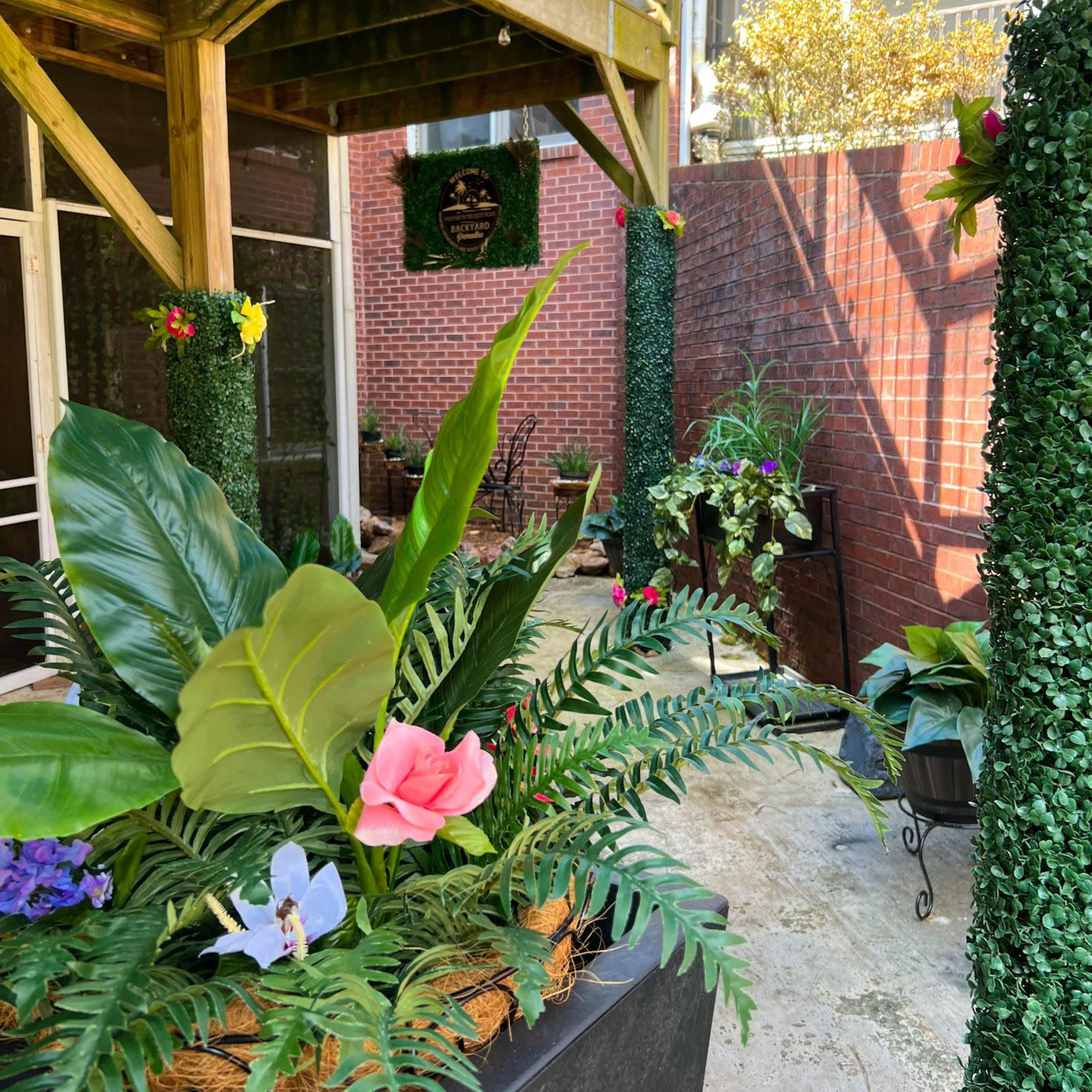 A garden space features various potted plants and vibrant flowers, bordered by brick walls and wooden structures.