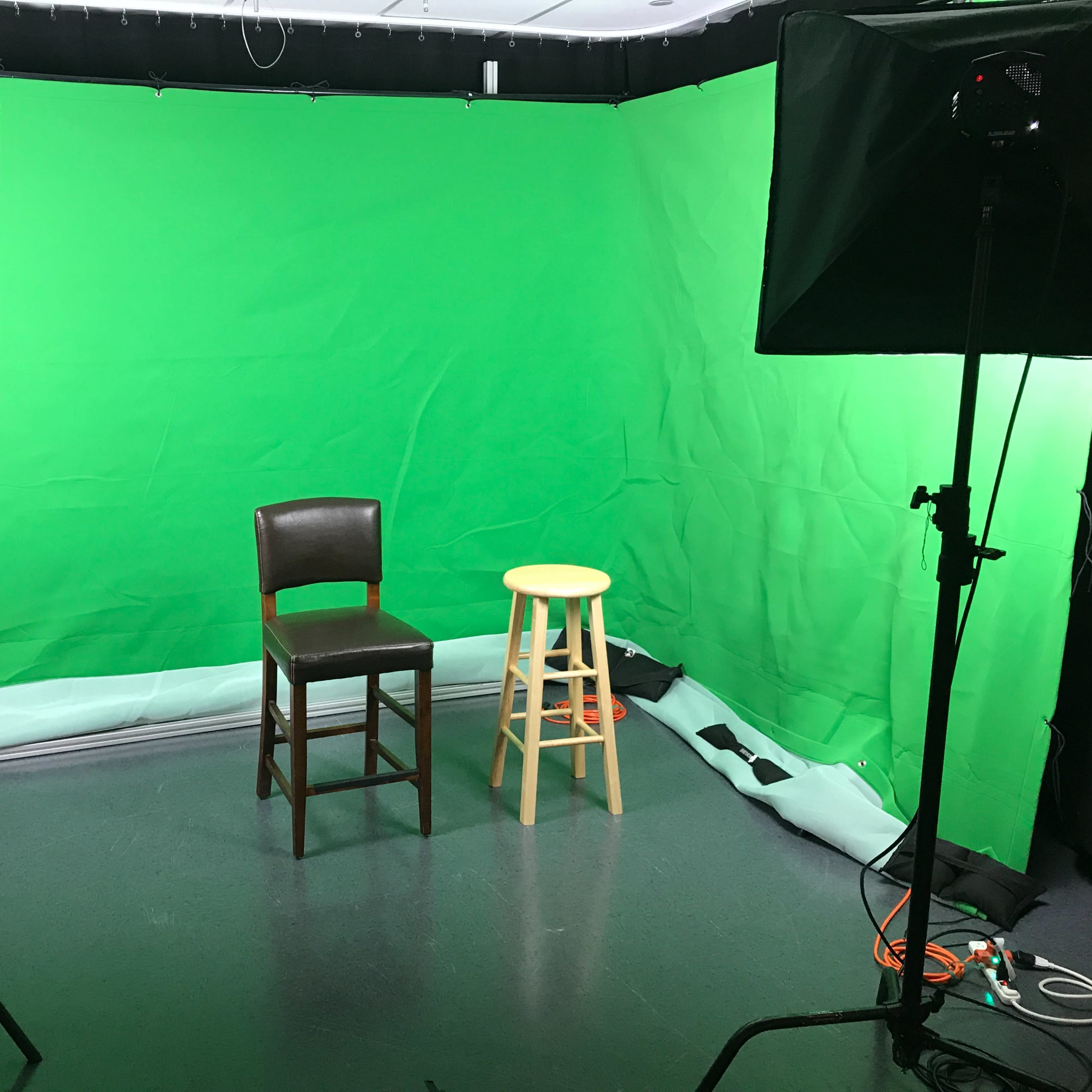A studio setup with a green screen backdrop, featuring a brown wooden chair and a yellow stool positioned in front of it.