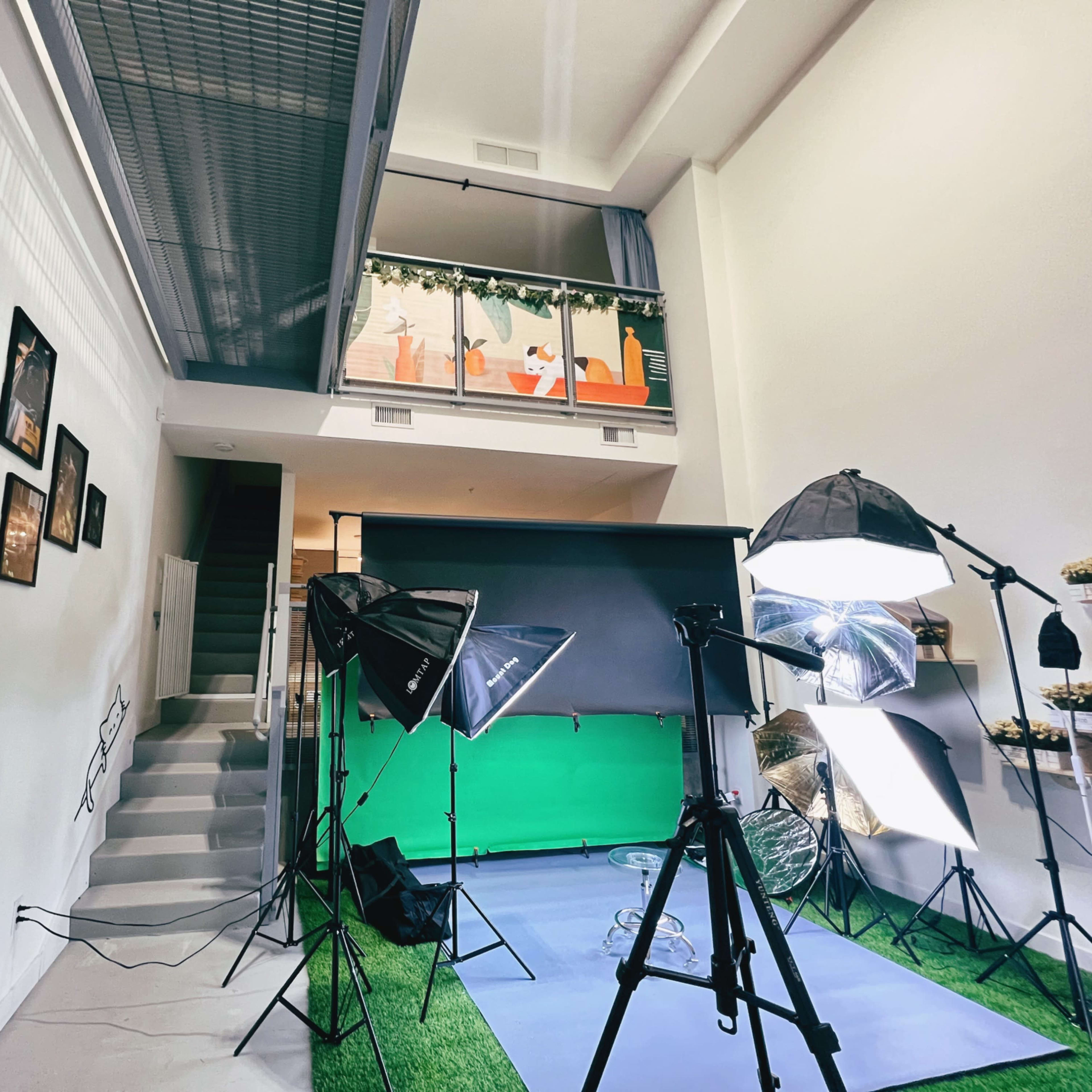 A photography studio setup with a green backdrop, lighting equipment, and a staircase leading to an upper level decorated with festive elements.