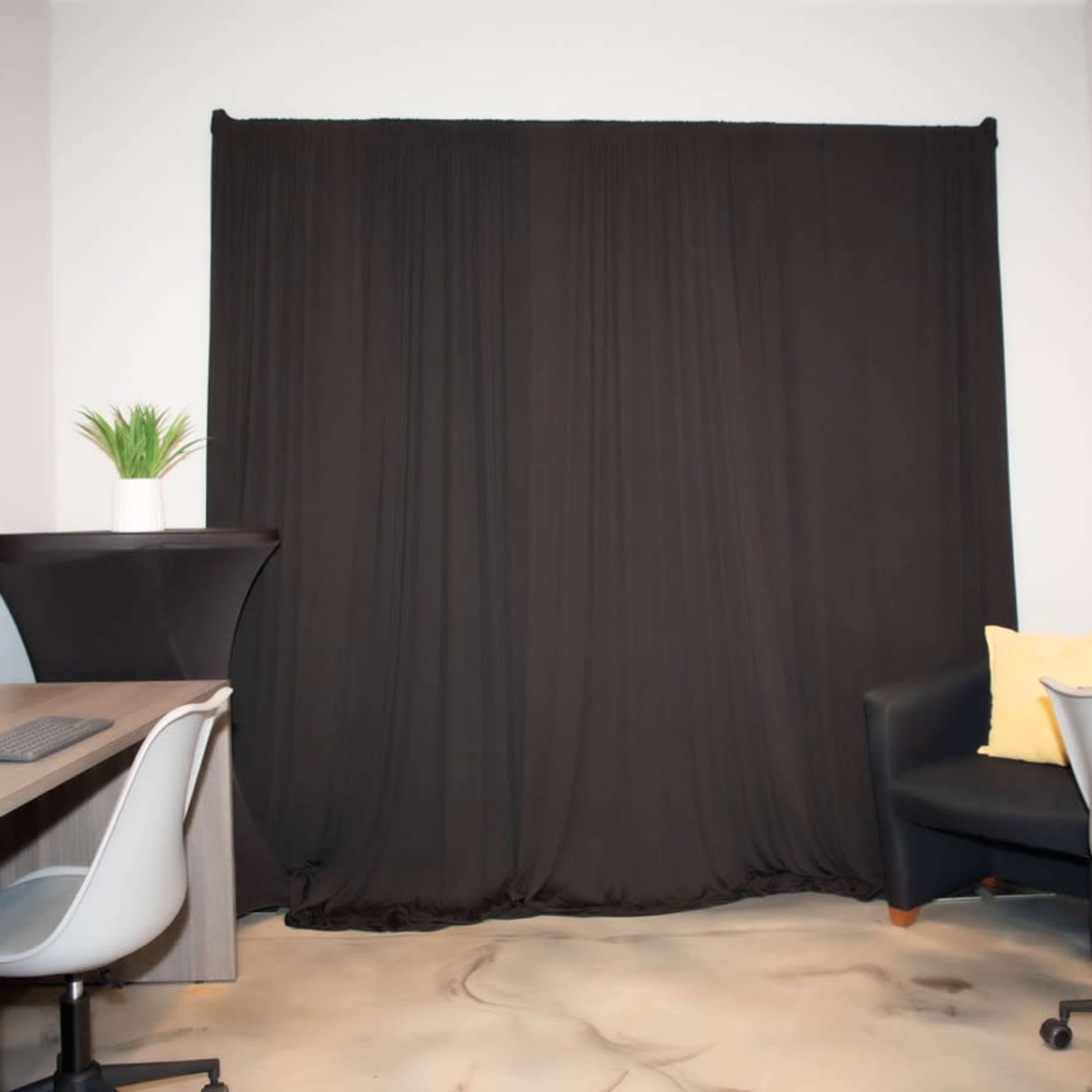 A room with two desks, a dark curtain in the center, and a black chair with a yellow pillow in a corner.