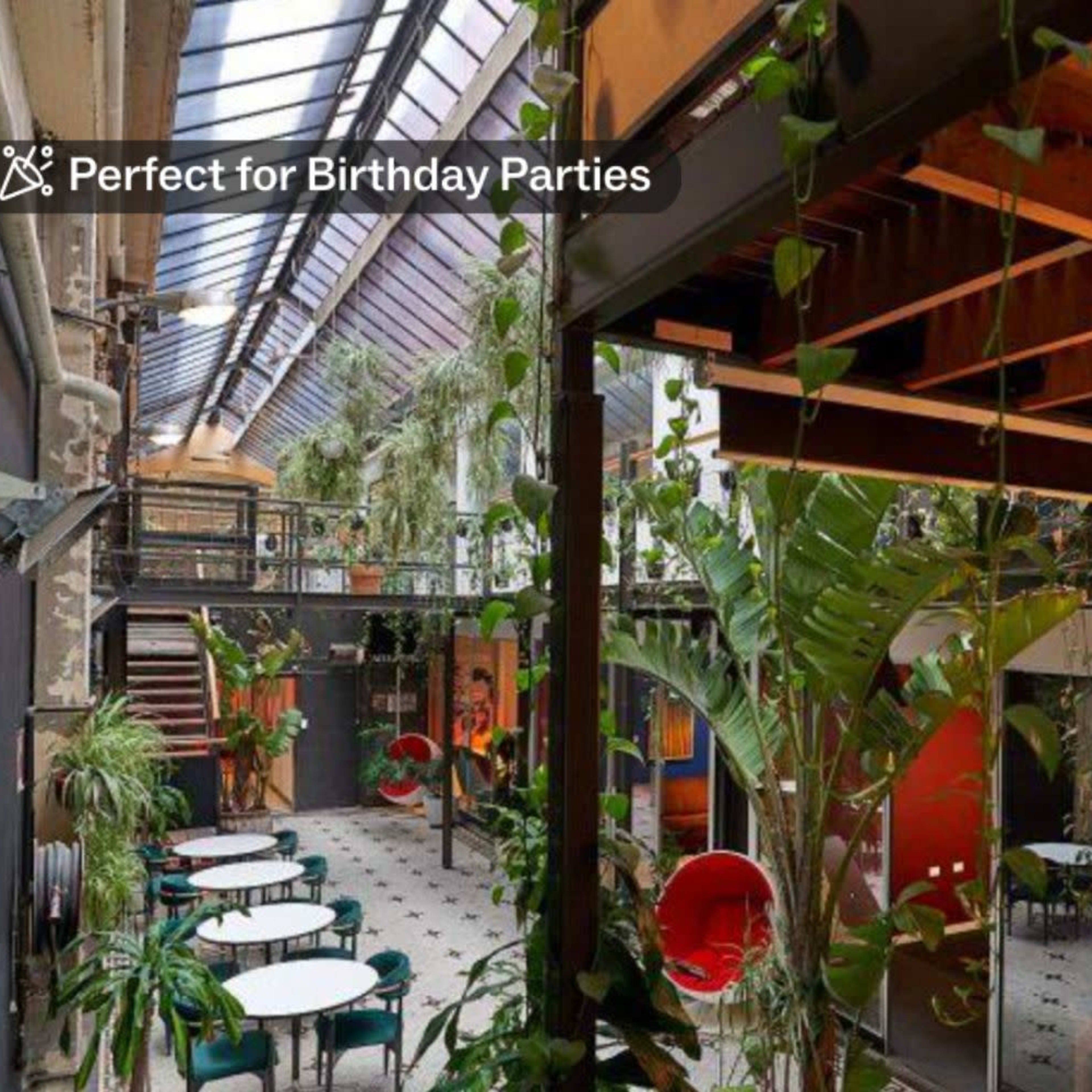A brightly lit indoor space filled with greenery, featuring dining tables and chairs arranged throughout.
