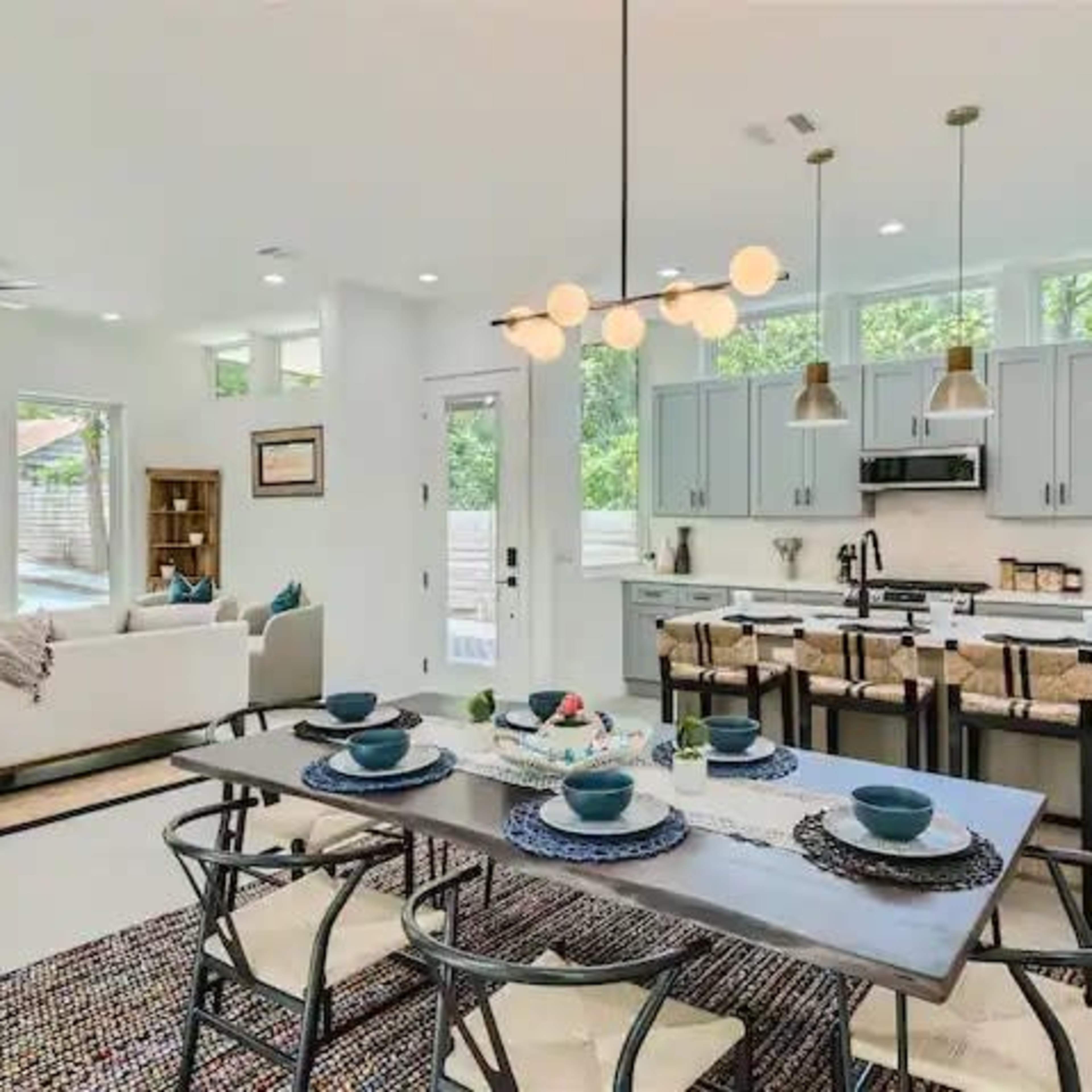 A modern kitchen and dining area with a wooden table set for a meal, surrounded by stylish chairs and light fixtures.