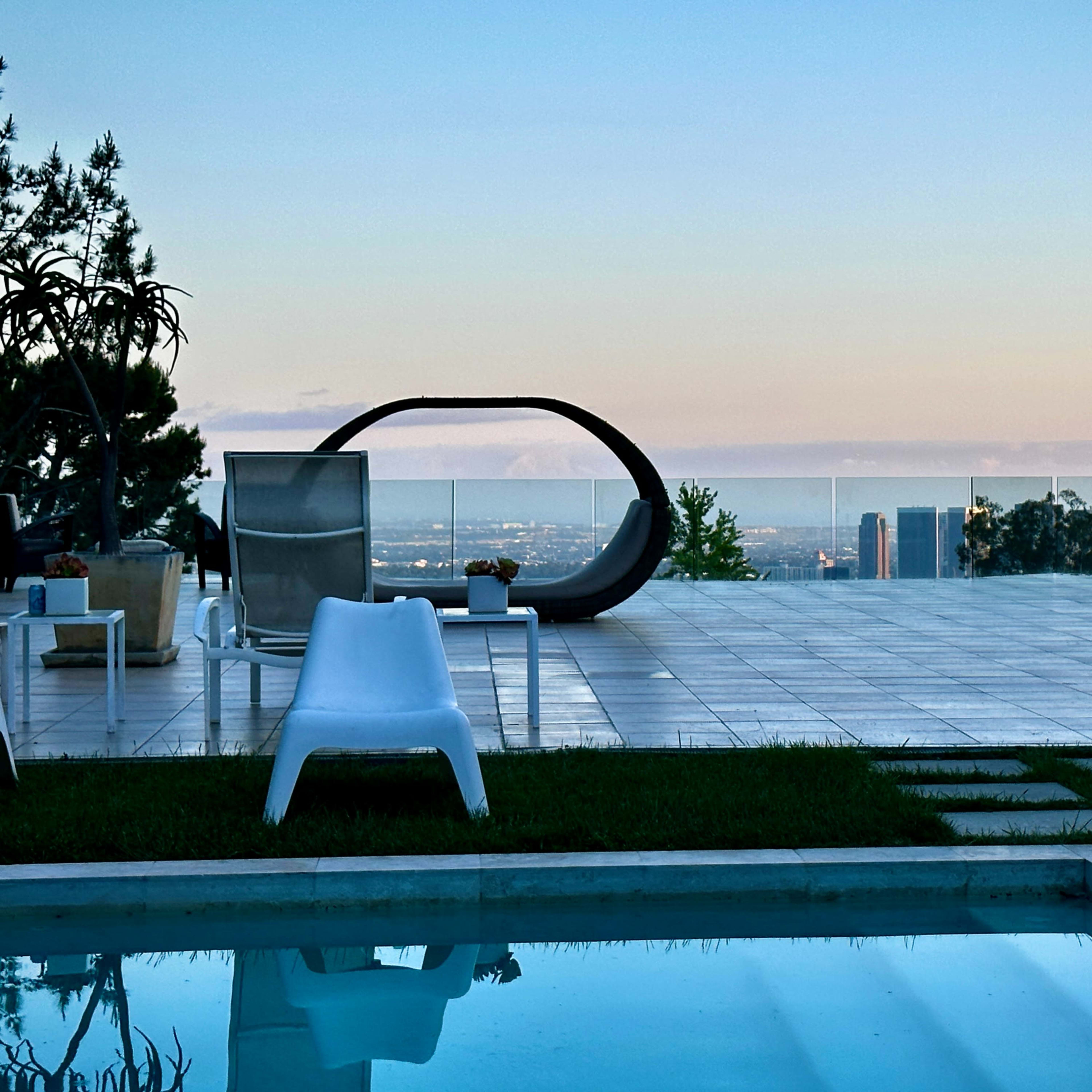 A terrace with modern outdoor furniture overlooking a city skyline and a swimming pool in the foreground.
