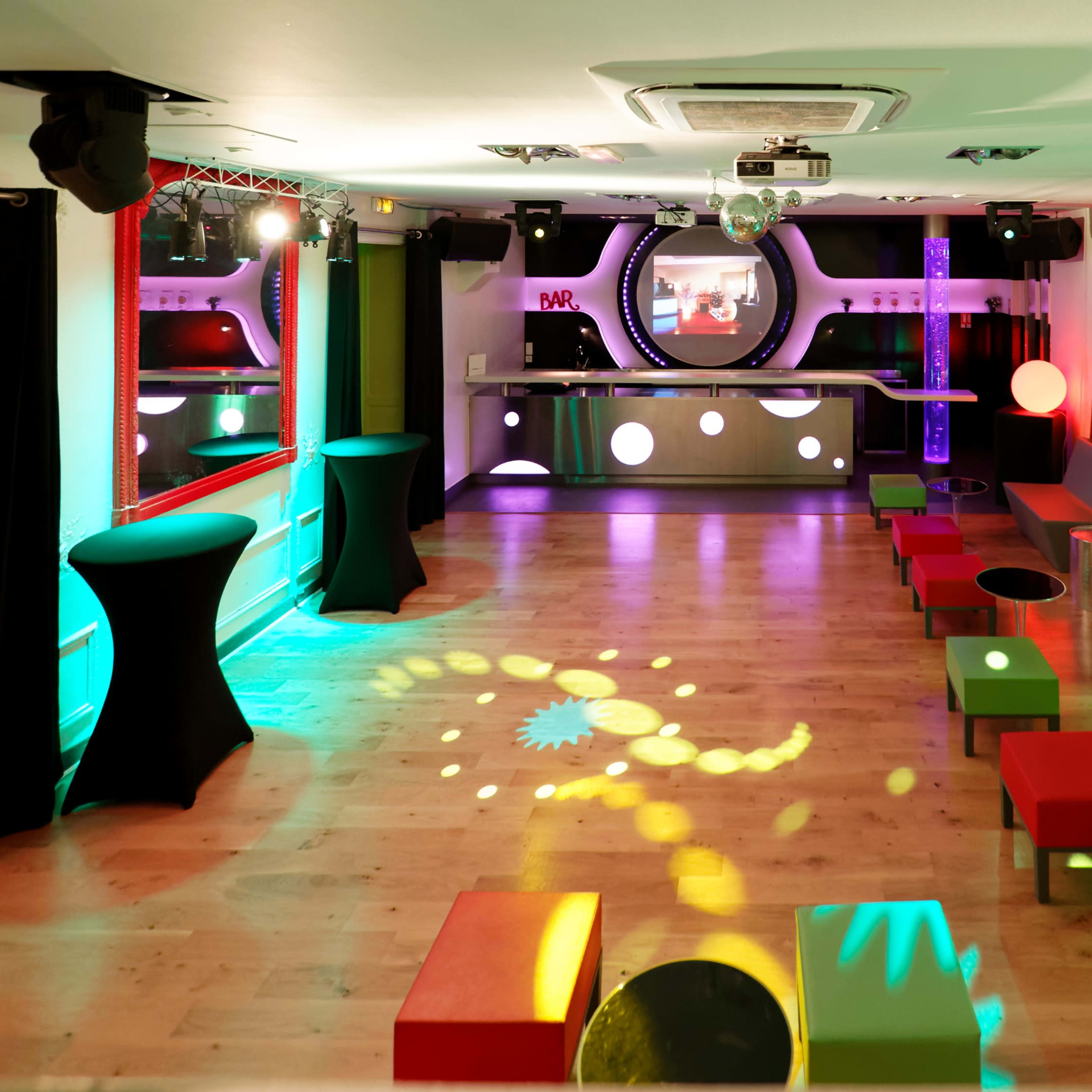 A brightly lit lounge area features colorful furniture and a bar in the background, designed for social gatherings and events.