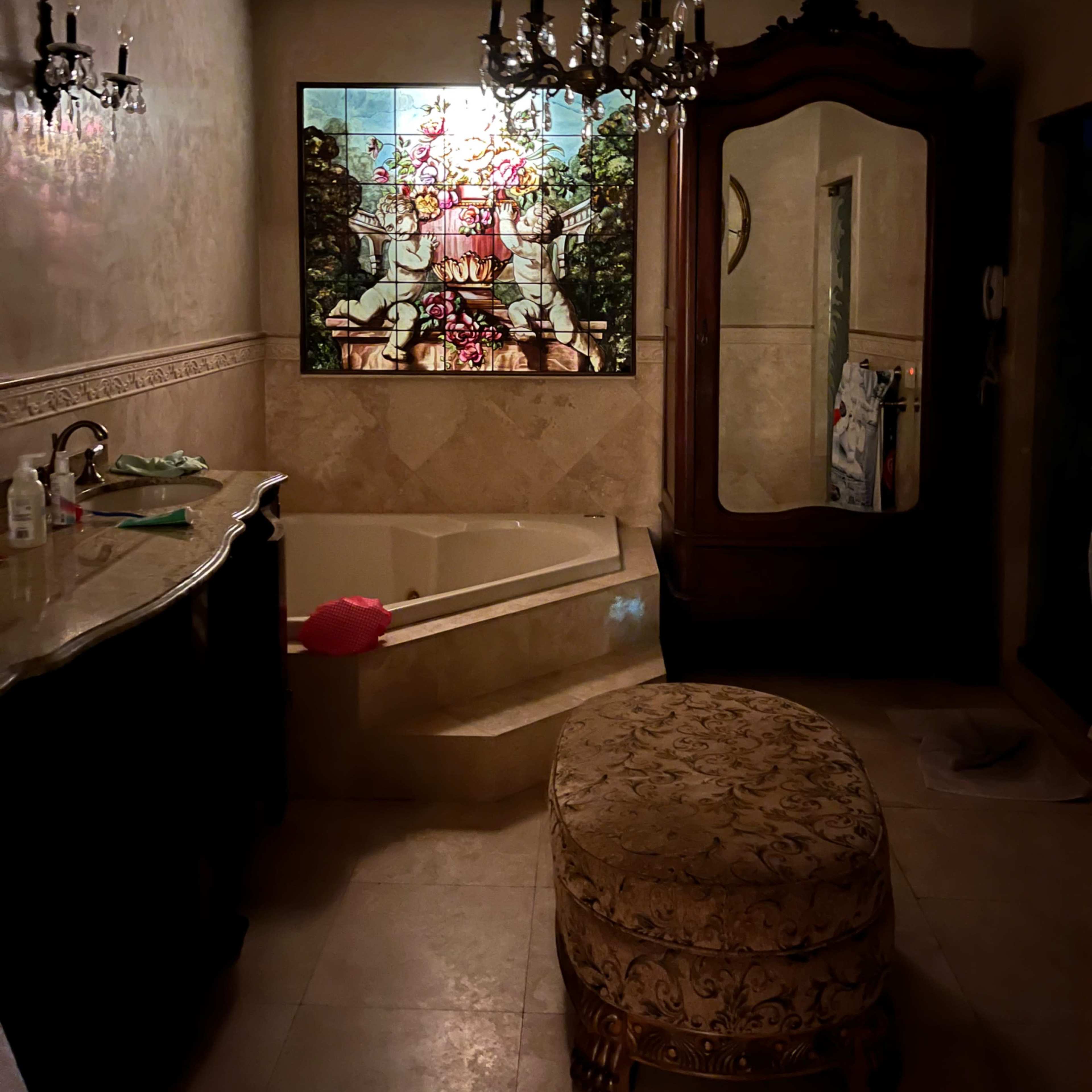 The bathroom features a large stained glass window, a freestanding bathtub, a chandelier, and an ornate mirror.