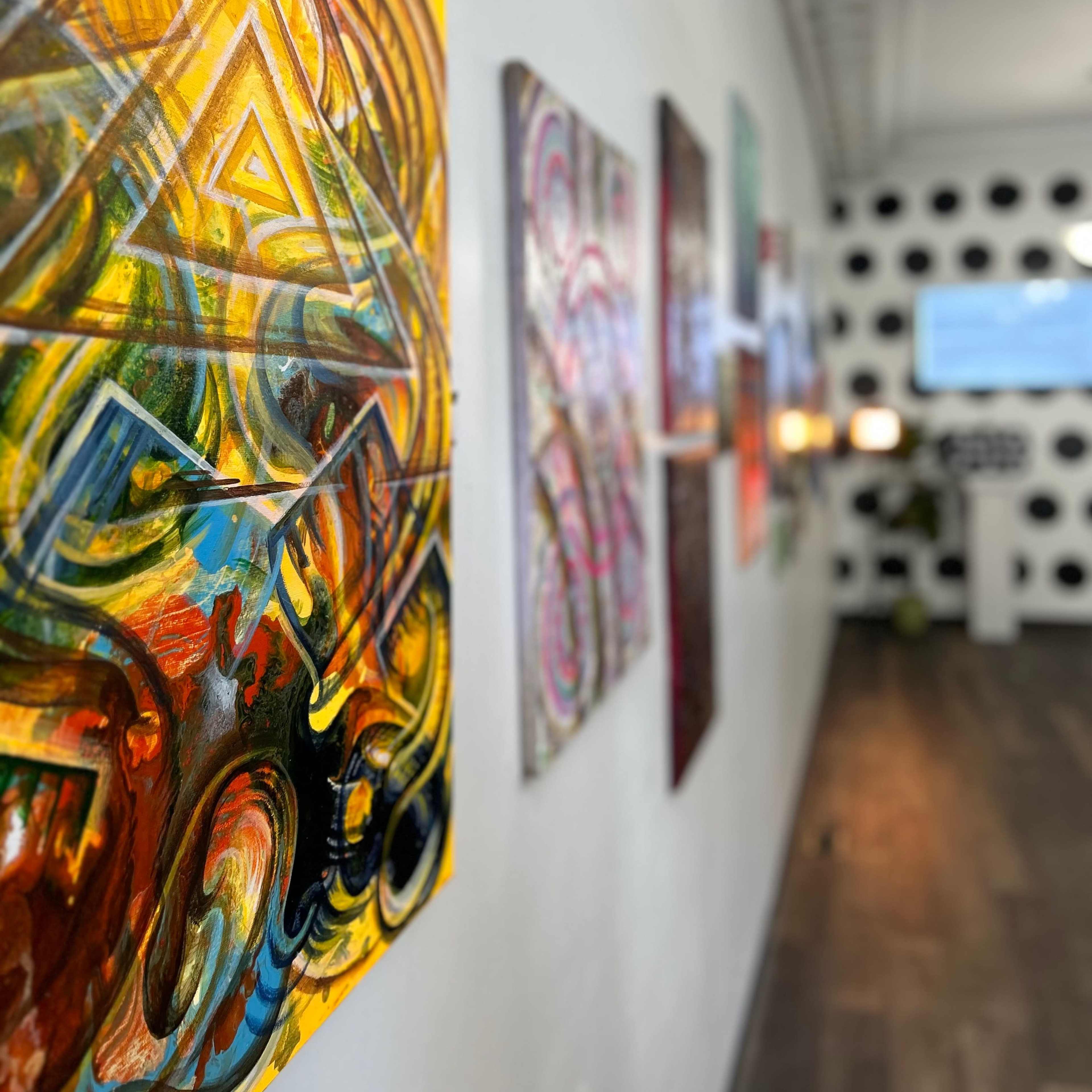 A gallery wall featuring colorful abstract paintings, with a blurred background of a room decorated with polka dots and modern furnishings.