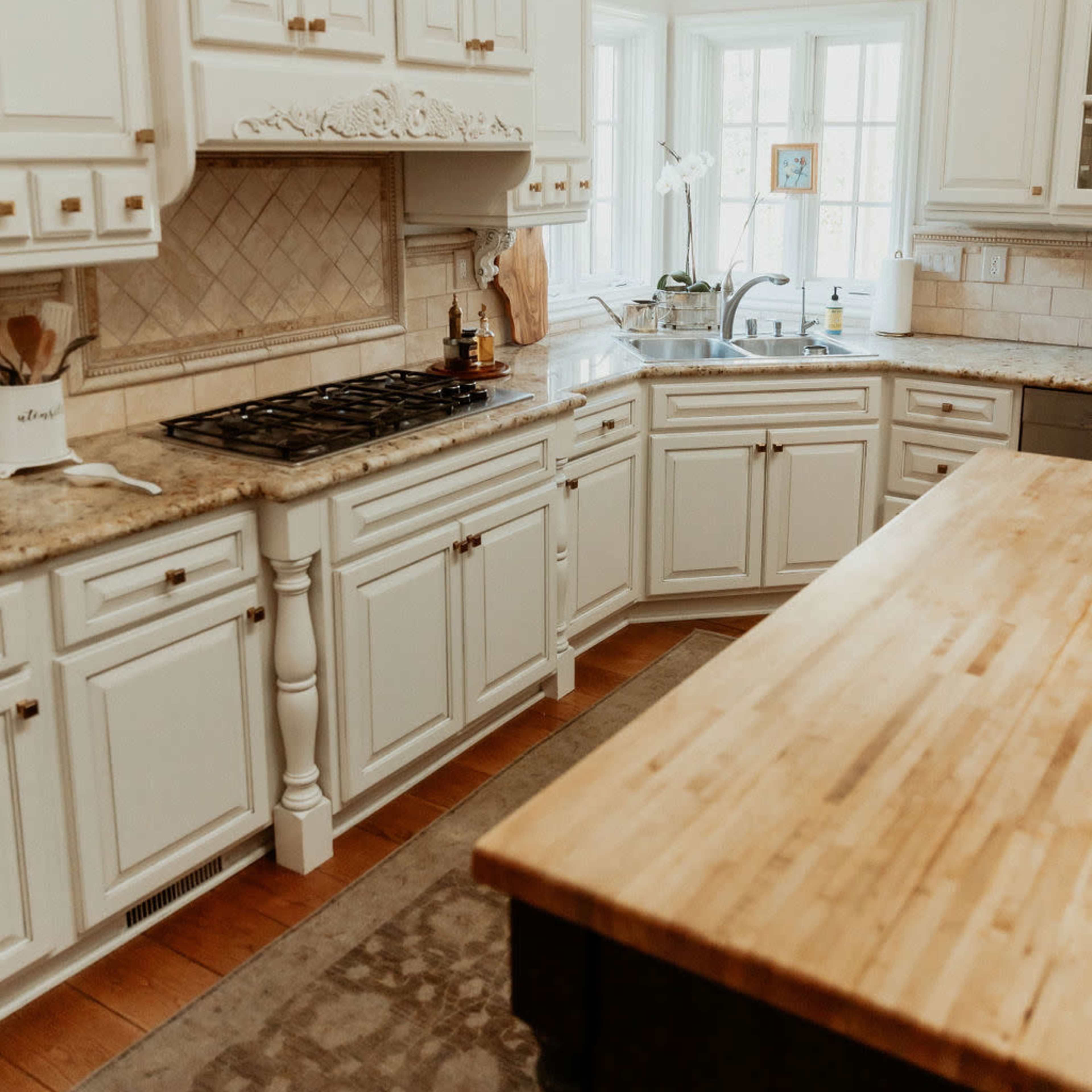 A bright kitchen features white cabinets, granite countertops, and a large wooden island.
