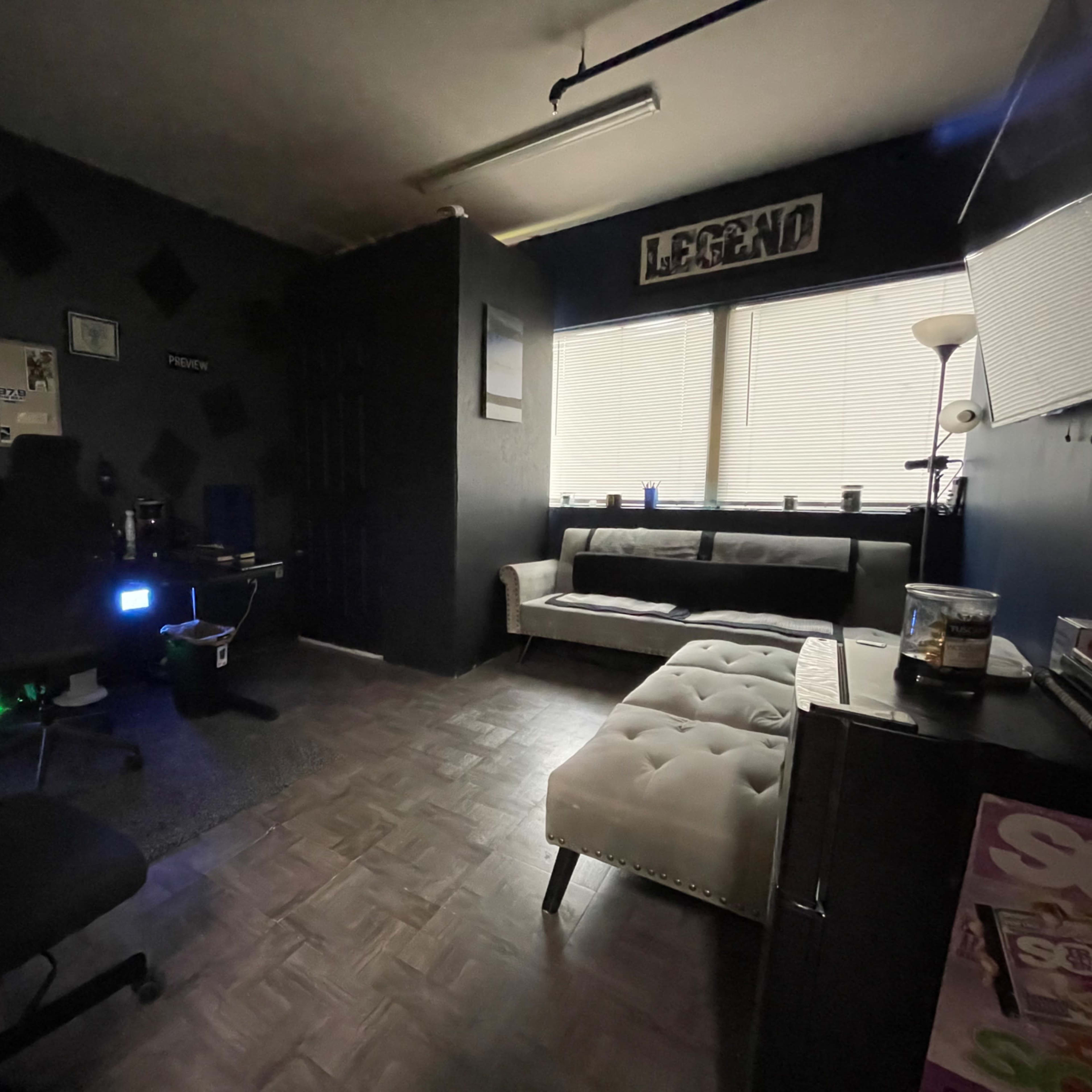 A small office space featuring dark walls, a desk with computer equipment, and a white couch against the wall.