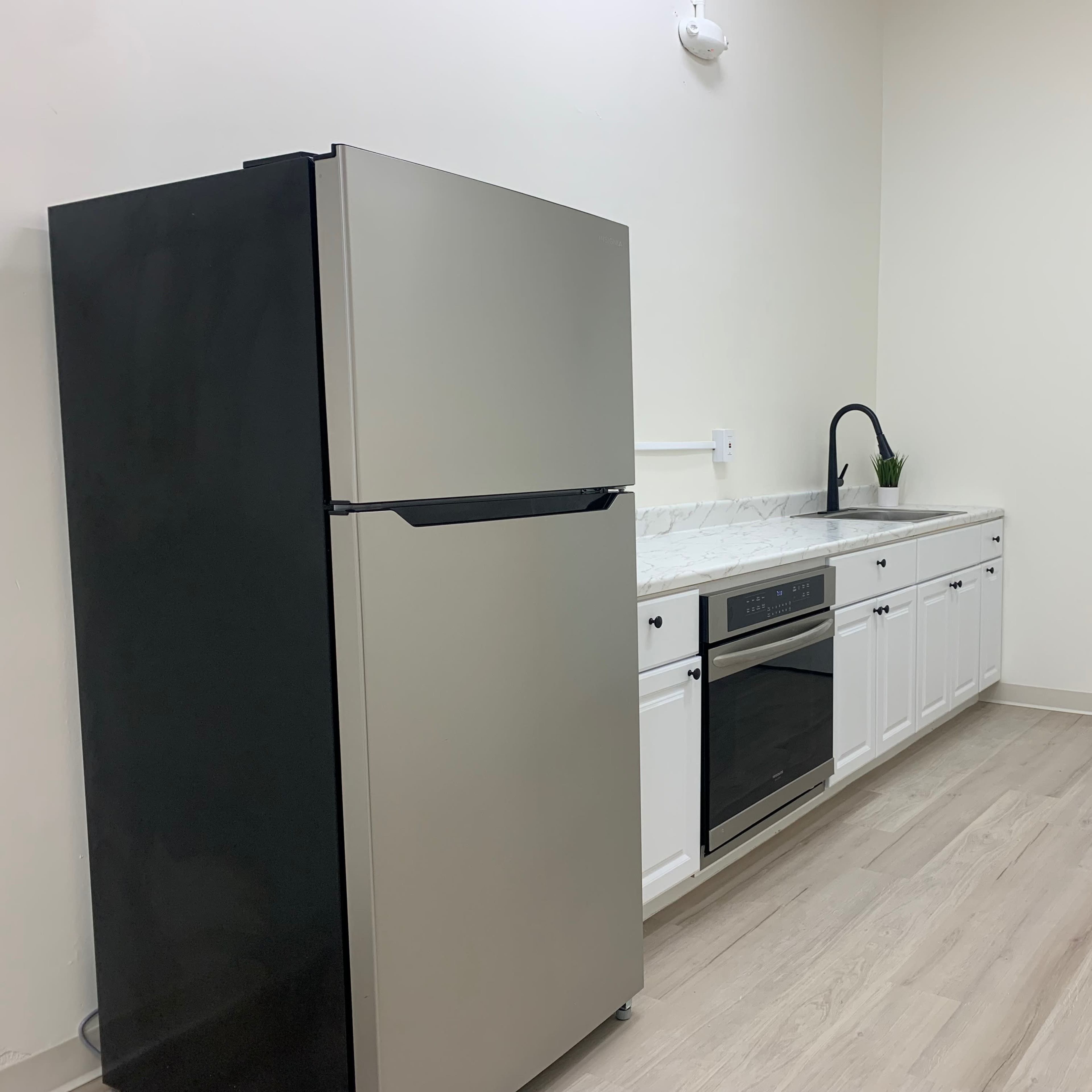 A modern kitchen featuring a stainless steel refrigerator, an oven, and white cabinetry, with a door labeled "EXIT" on the back wall.