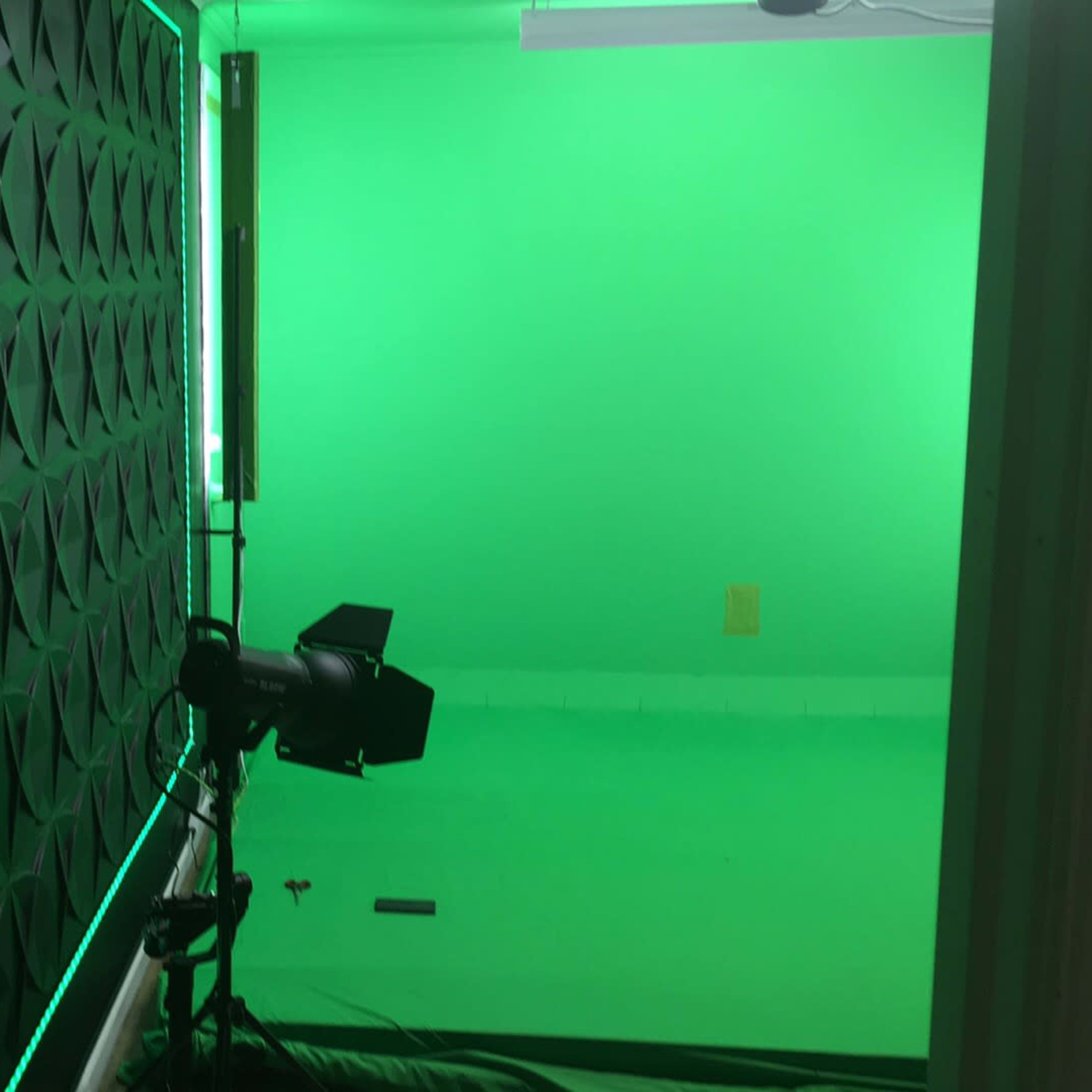A green screen studio with a textured black wall and lighting equipment set up against a green background.