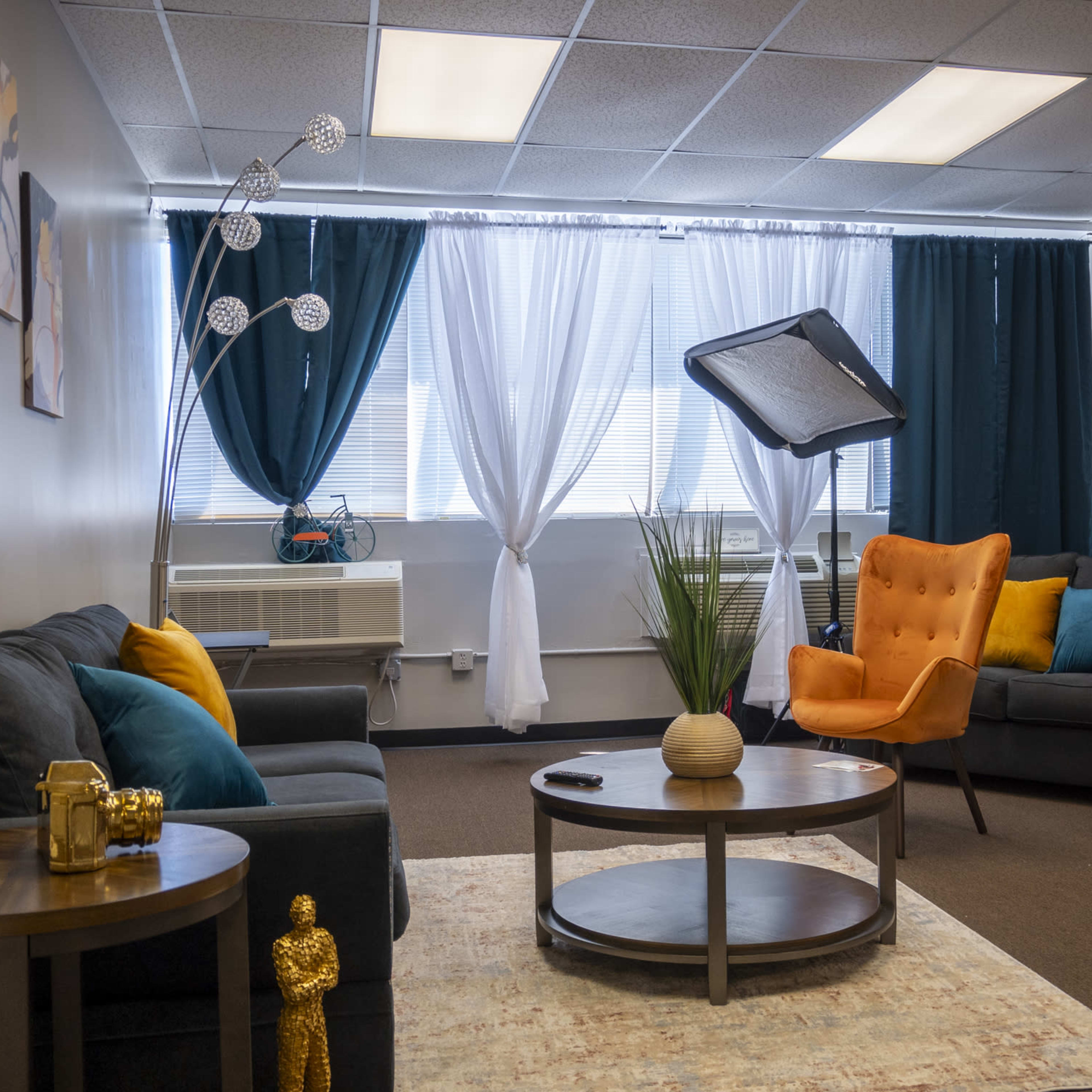 A modern waiting area featuring two armchairs, a sofa, a round coffee table, and large windows with sheer curtains.
