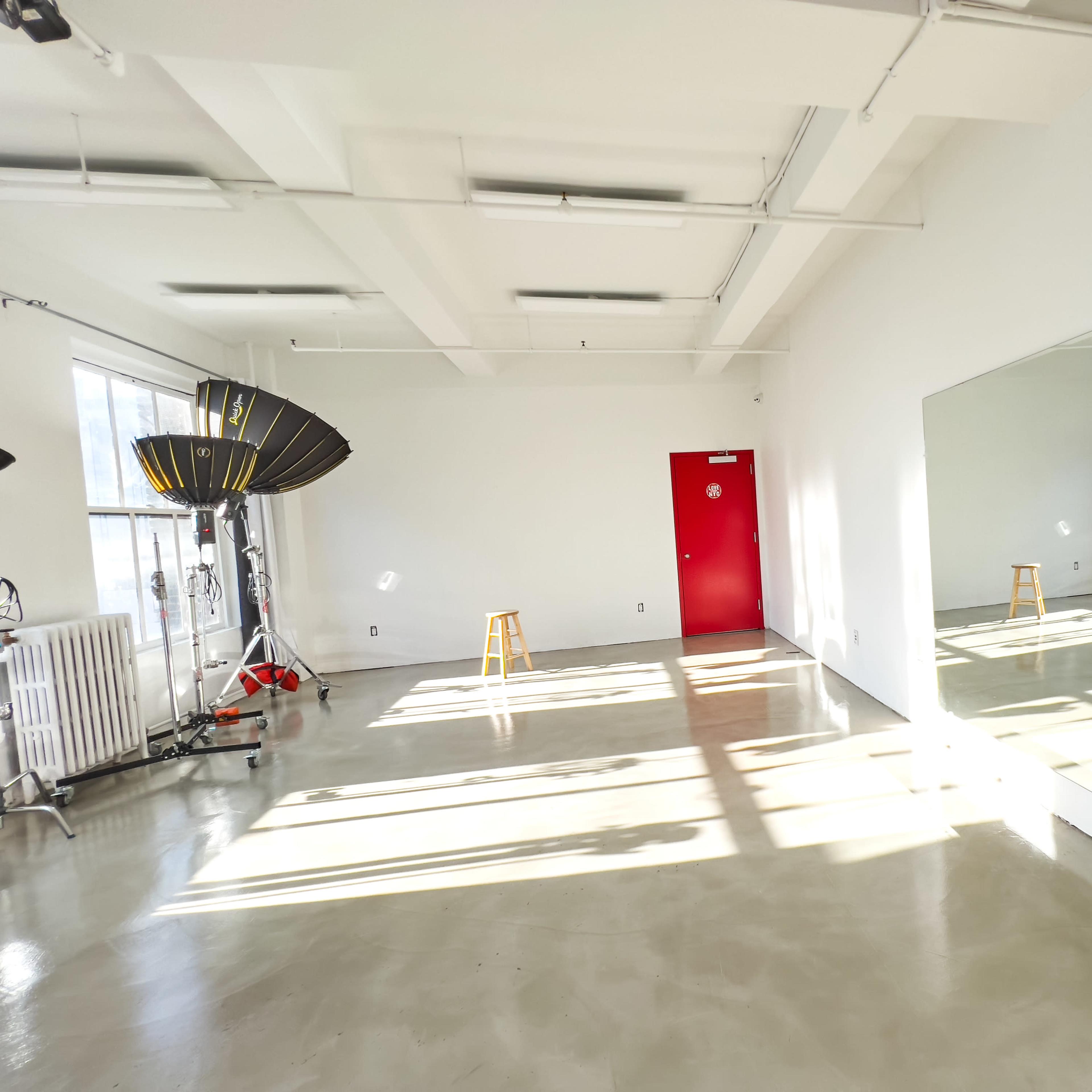 A spacious, well-lit studio with a red door, large mirror, and photography equipment set up on either side.
