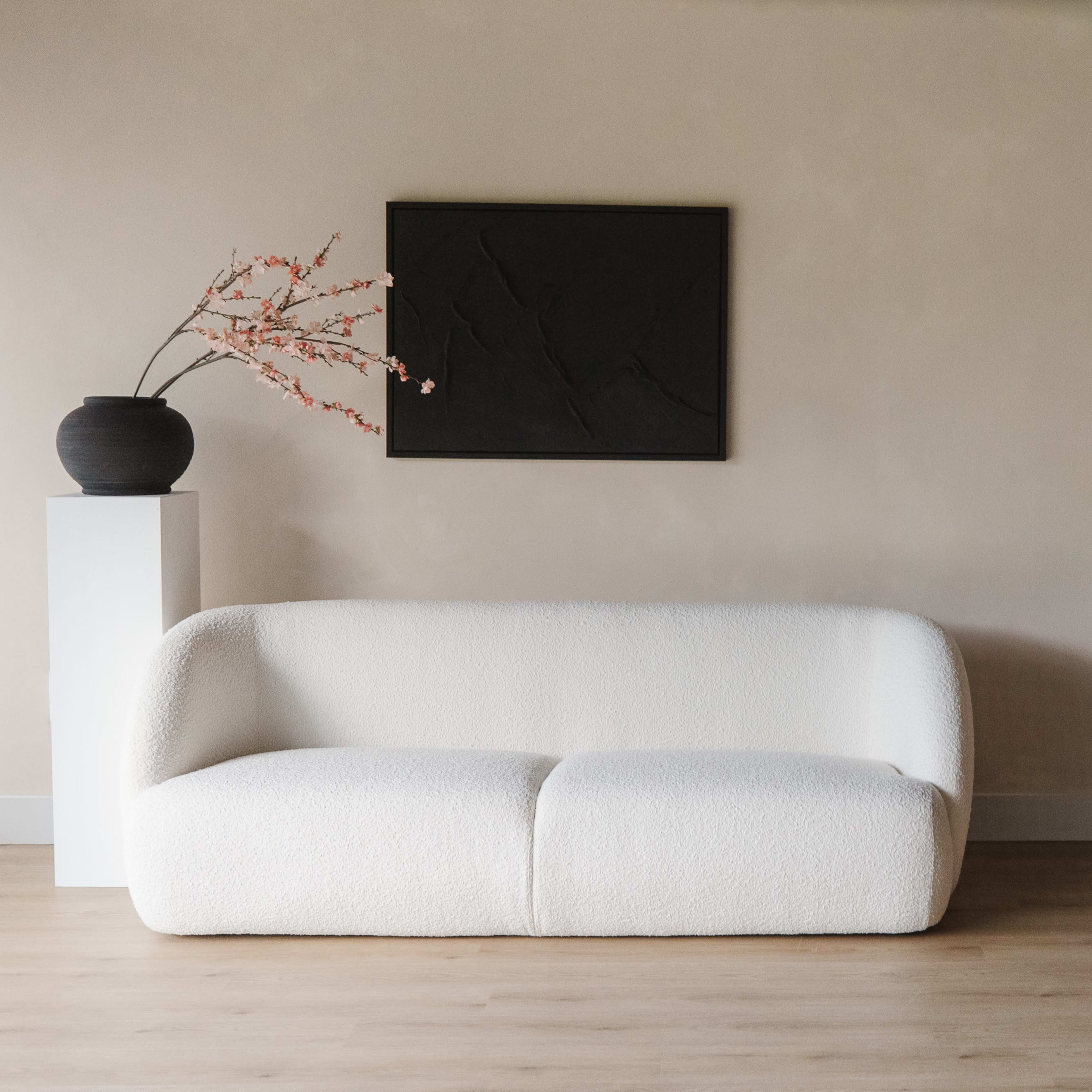 A white, upholstered sofa is positioned against a light wall, accompanied by a black framed artwork and decorative vases with branches.