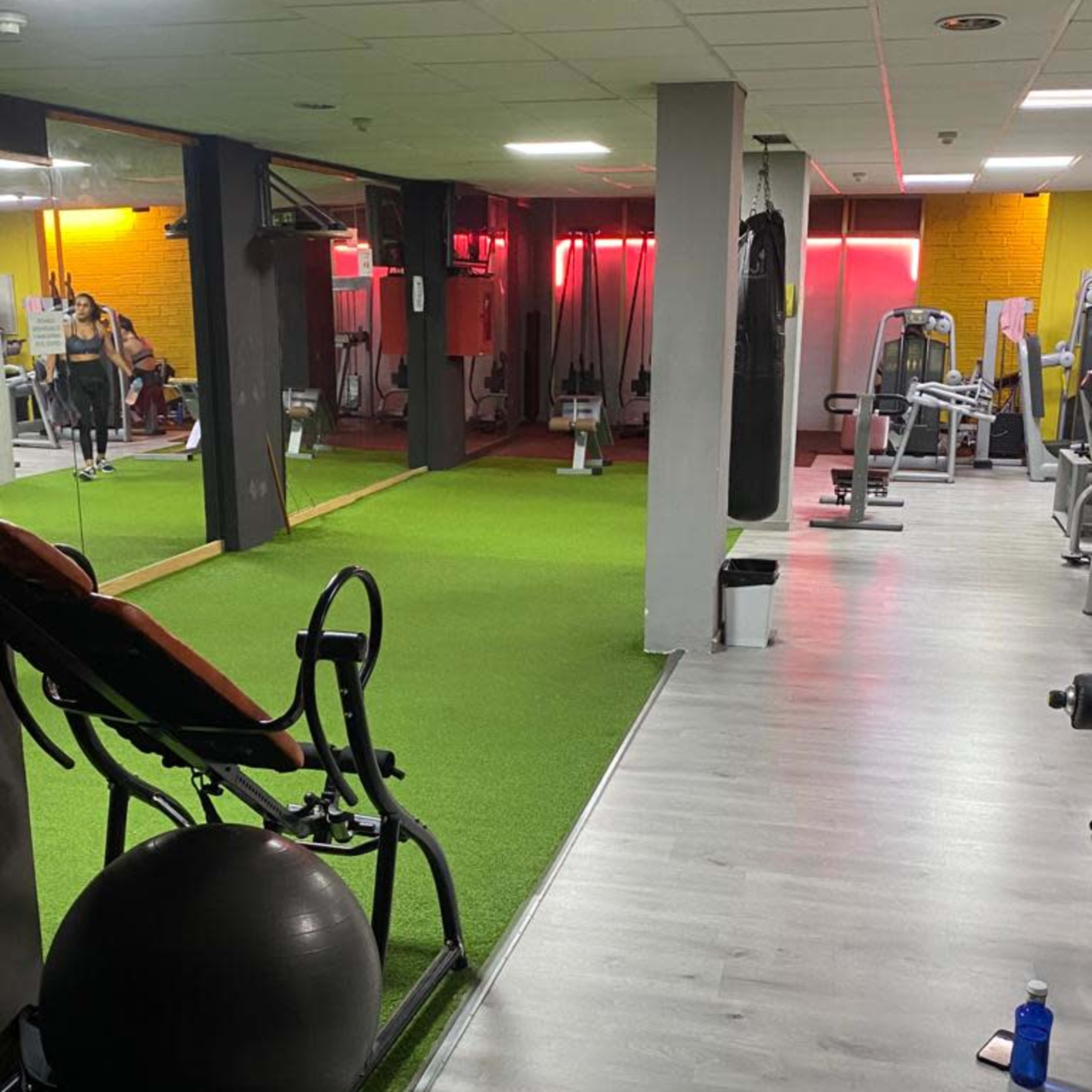 A gym interior with green turf flooring, exercise equipment, and dim lights in the background.