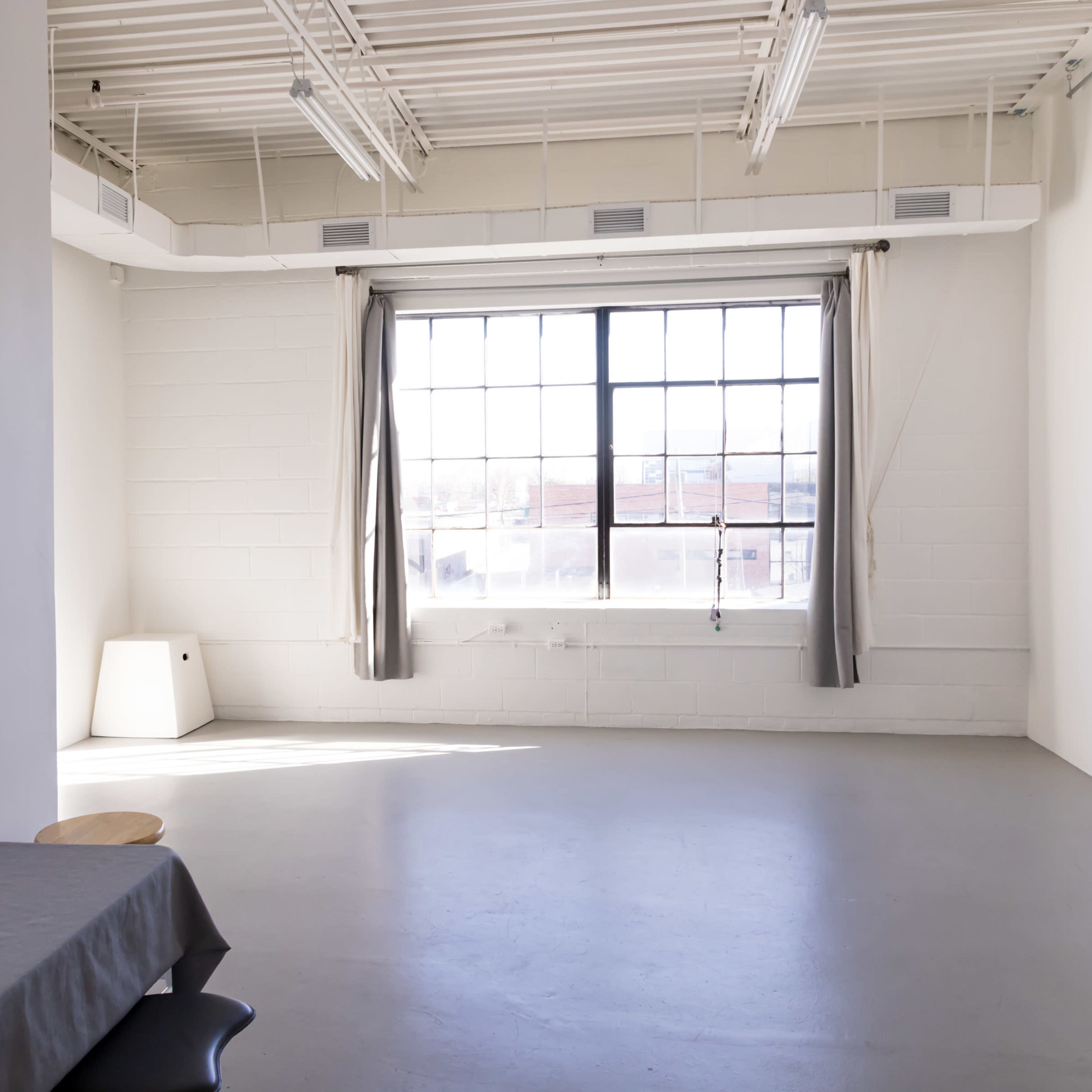 A spacious, well-lit room with a large window, a table, and minimal furnishings.