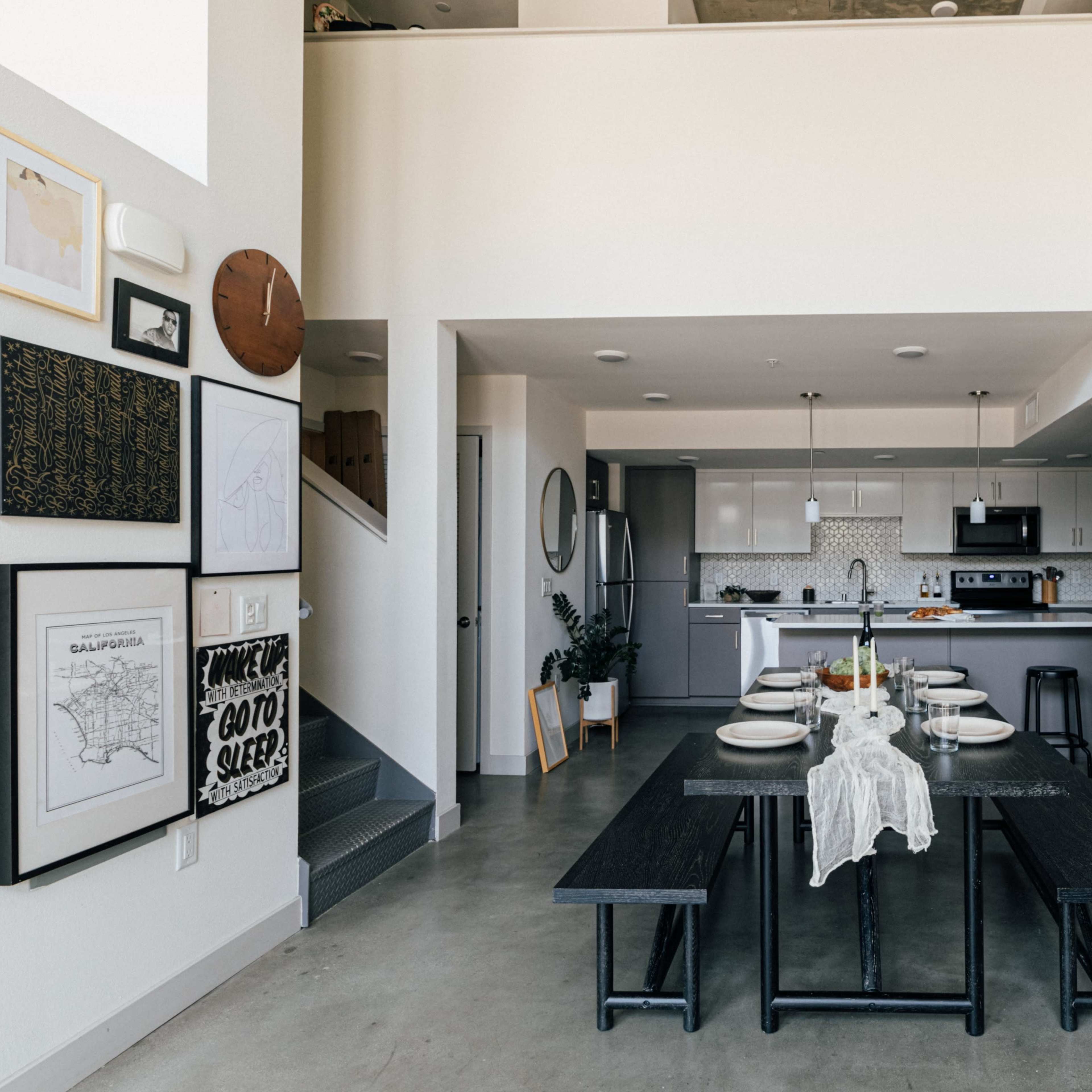 A modern dining area with a large black table set for a meal, adjacent to an open kitchen featuring cabinets and appliances.