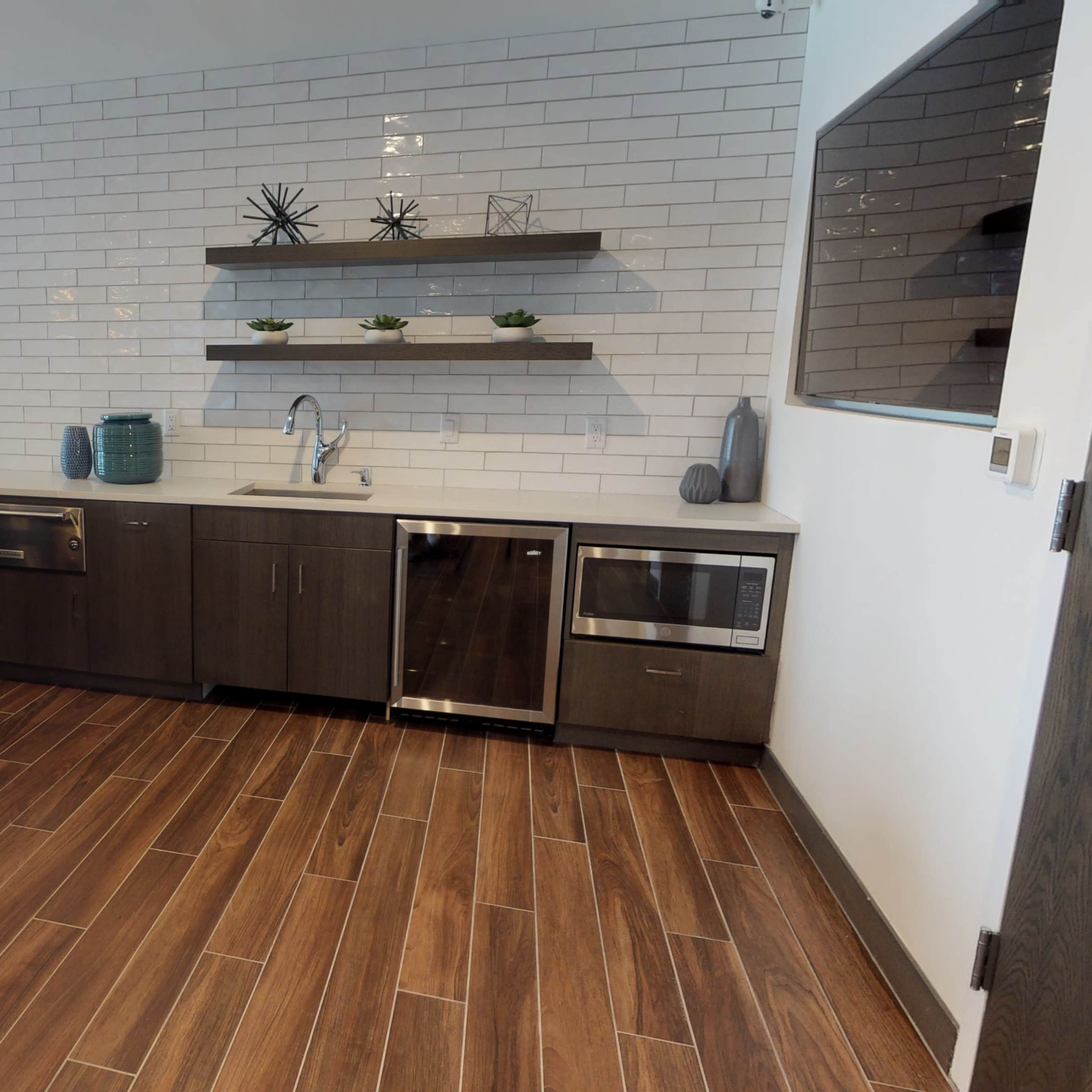 A modern kitchen with dark wooden cabinetry, a countertop bar with stools, and a tiled wall featuring decorative shelves.