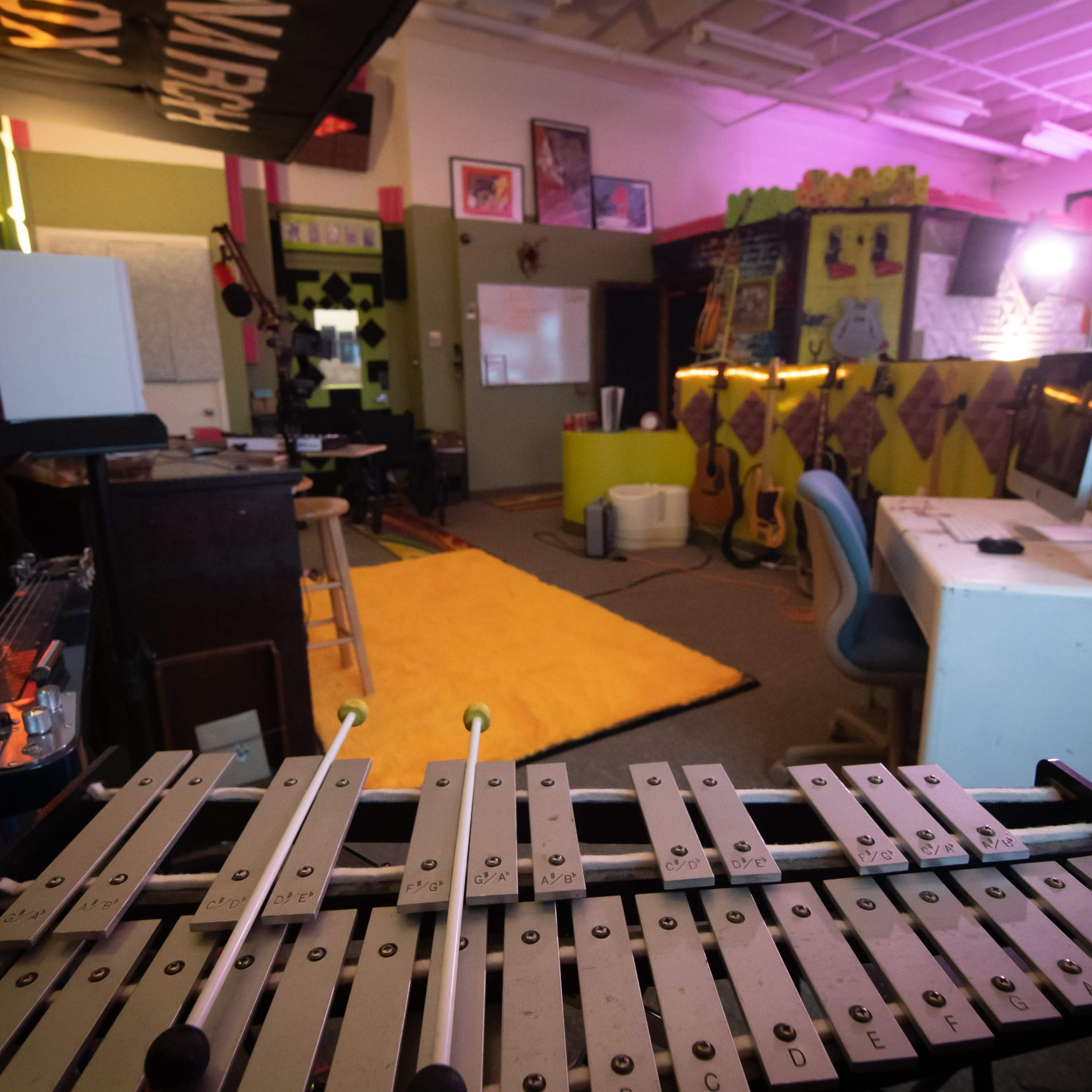 A colorful room with musical instruments, including a xylophone in the foreground, and various art pieces and furniture arranged throughout the space.