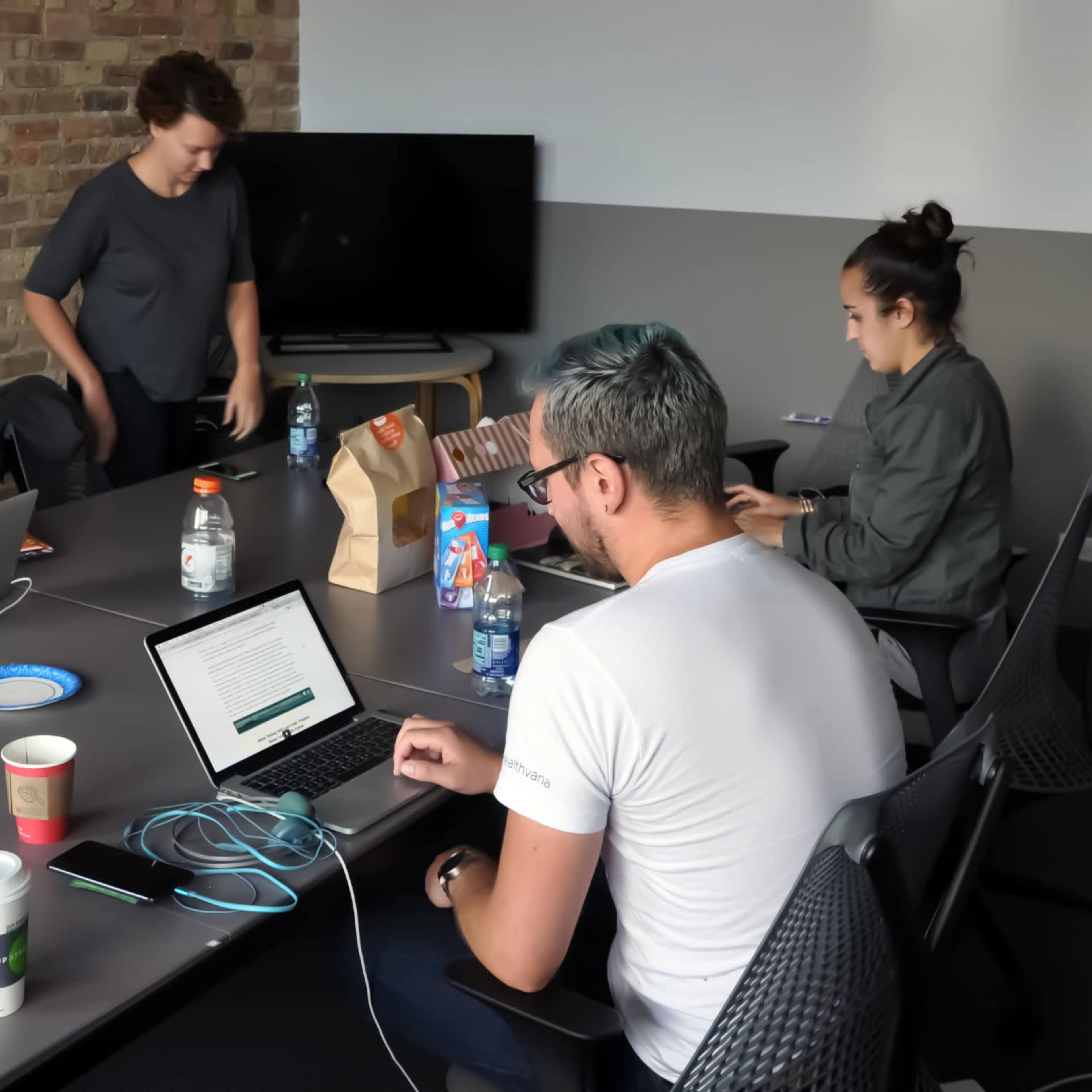 A group of four people is working on laptops at a conference table in a modern office space.