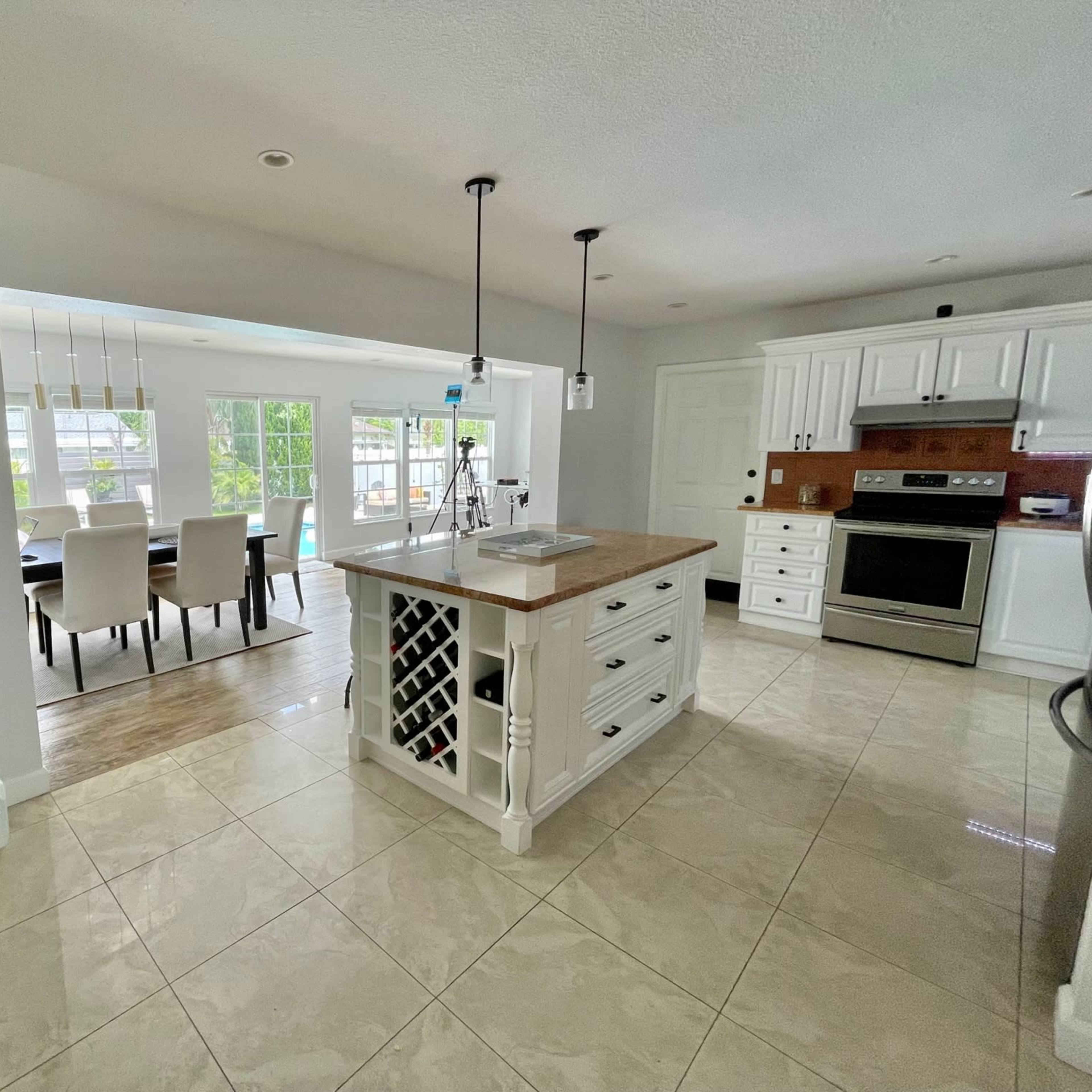 A modern kitchen with white cabinetry, a central island with a wooden top, and an adjoining dining area featuring a table and chairs.