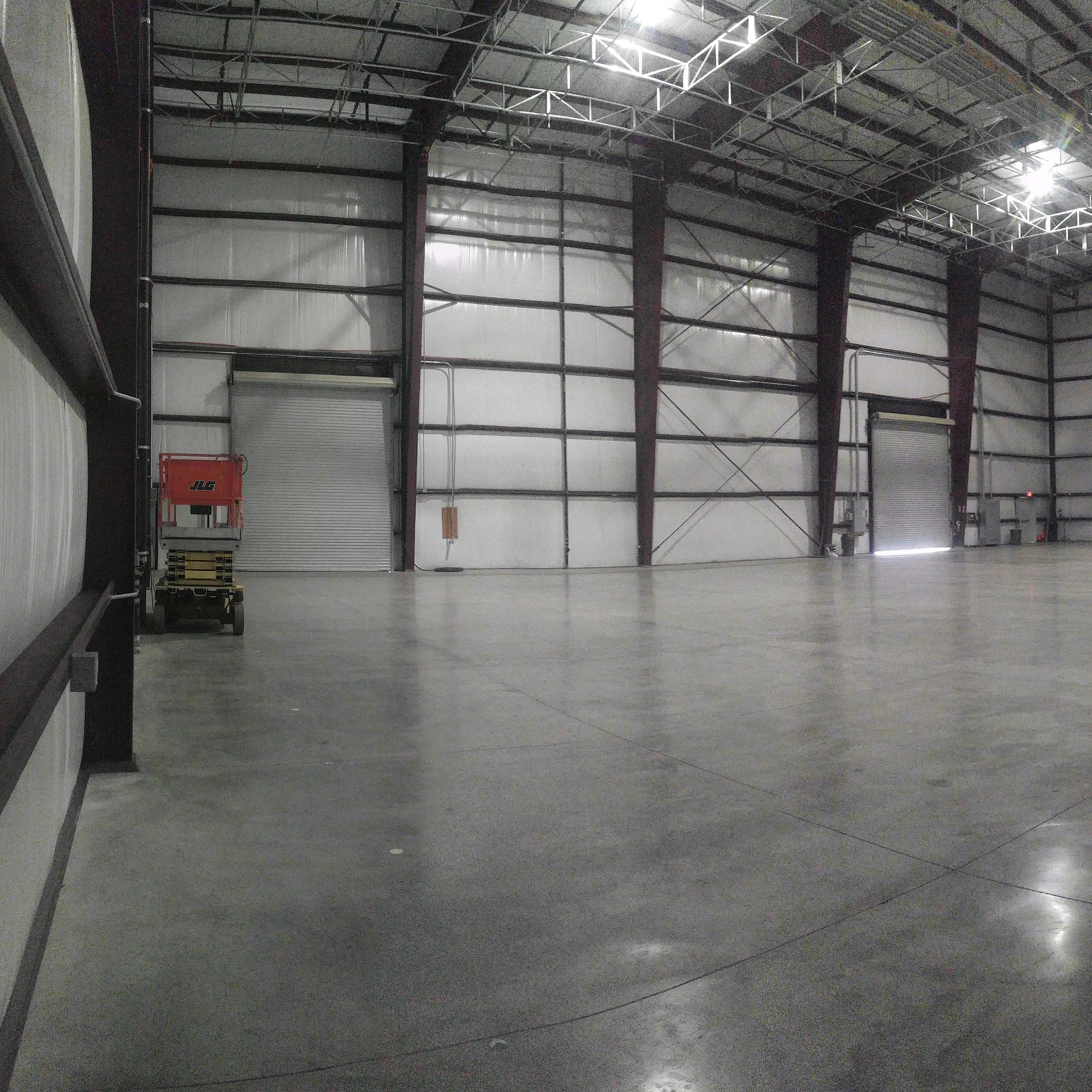 A large, empty industrial warehouse with high ceilings and a smooth concrete floor.