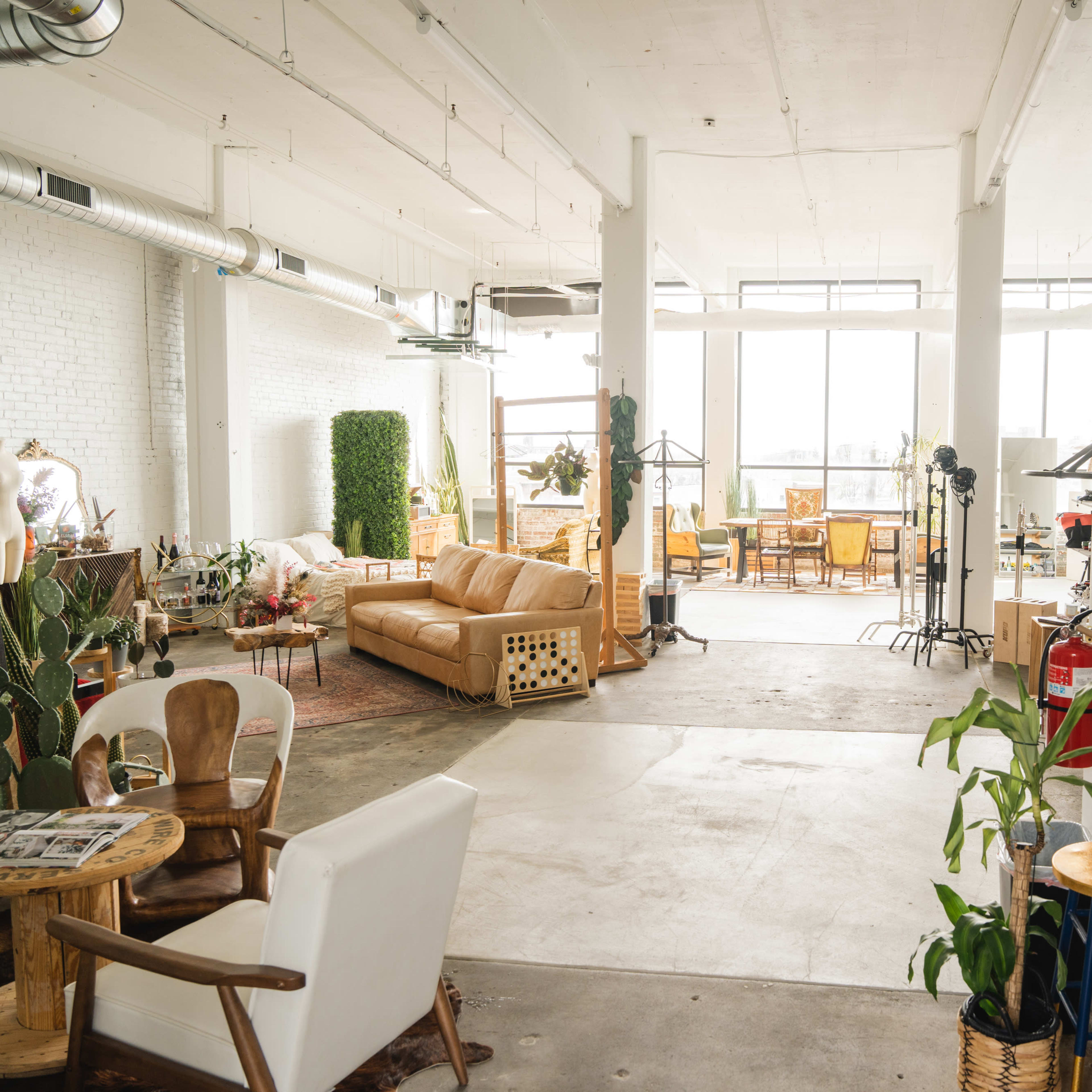 A spacious, well-lit studio with various pieces of furniture and décor, including a sofa, chairs, and plants.
