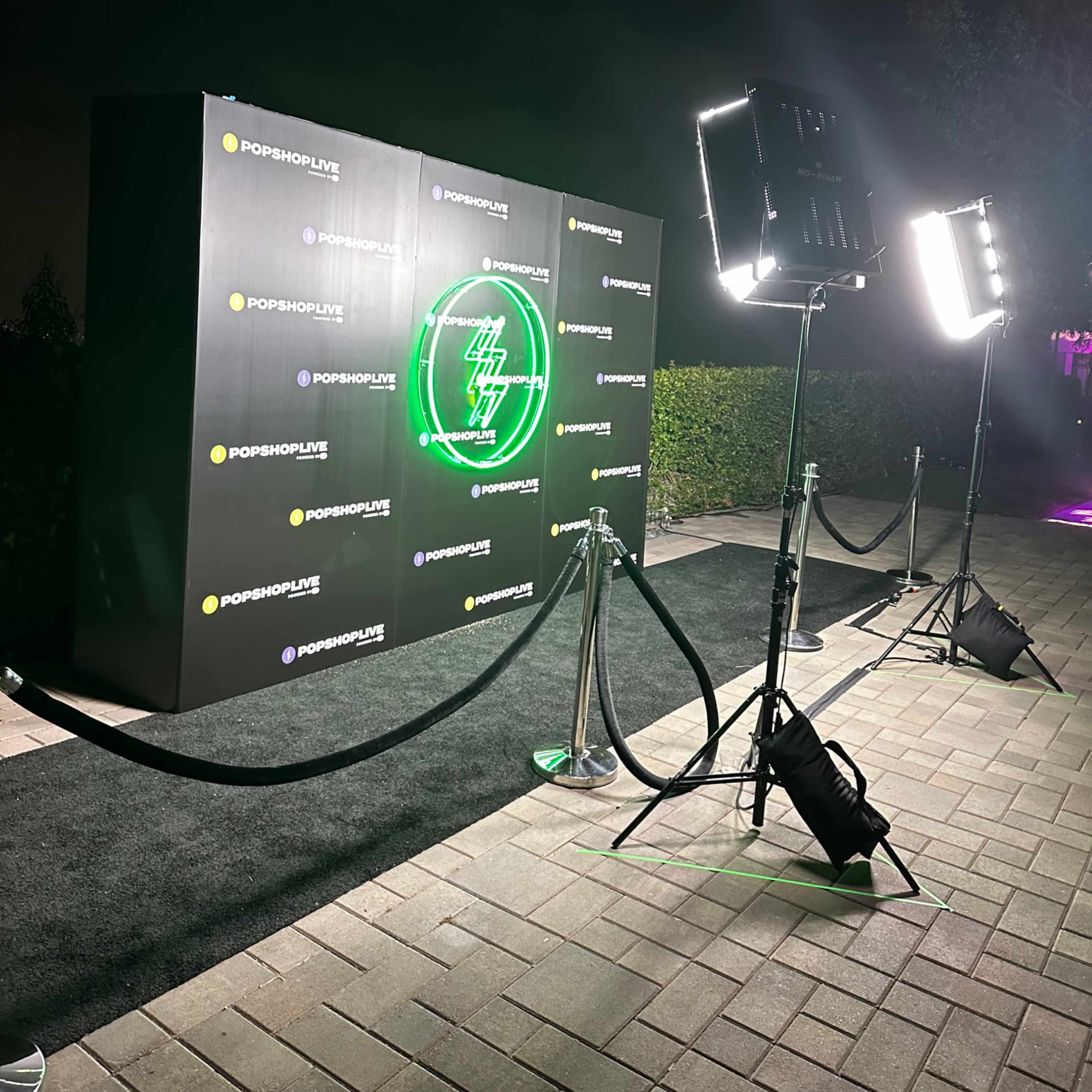 A black backdrop with a neon logo, illuminated by bright lights, in front of a red carpet area.