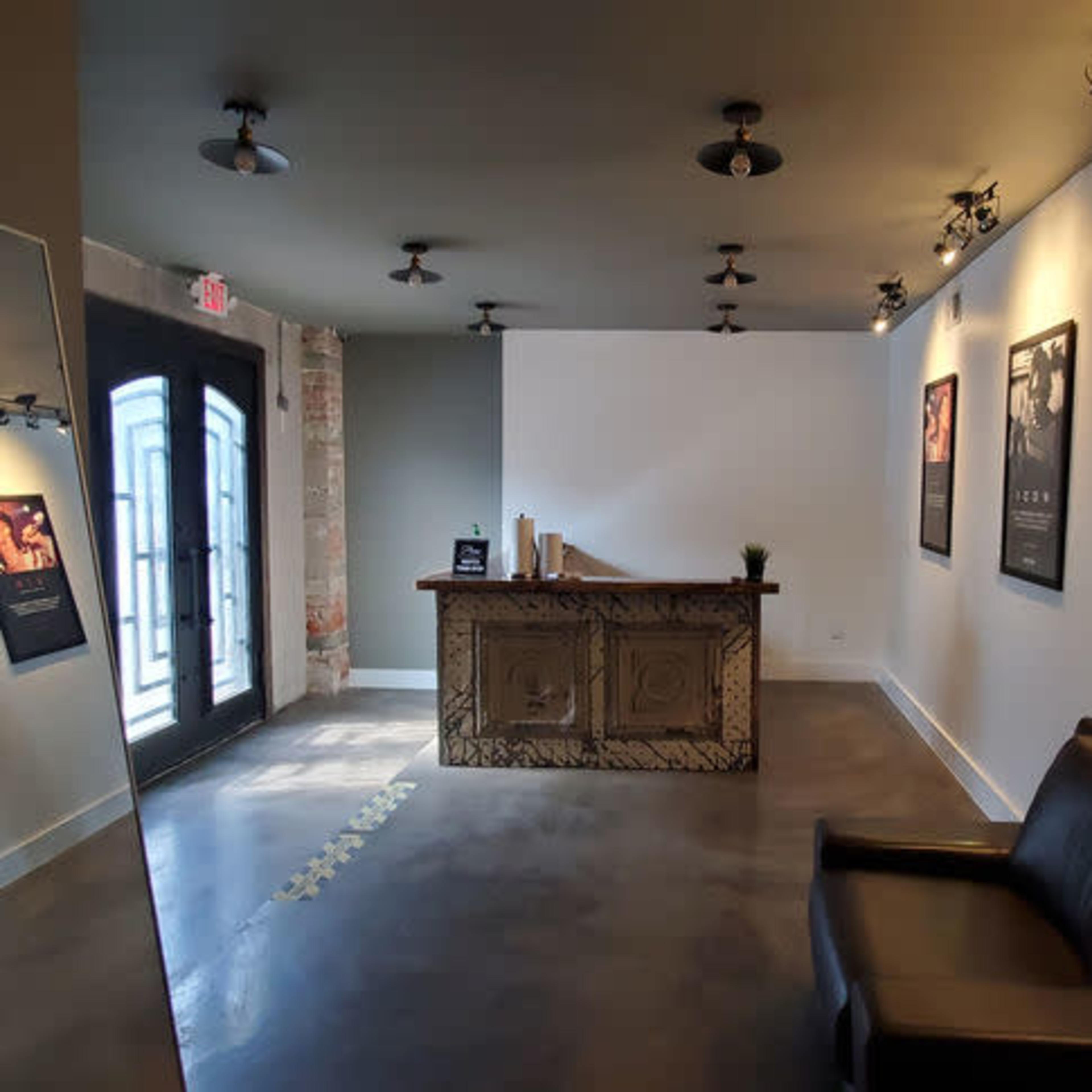 A modern reception area featuring a wooden front desk, a black leather chair, and movie posters on the walls, with a large mirror reflecting the space.