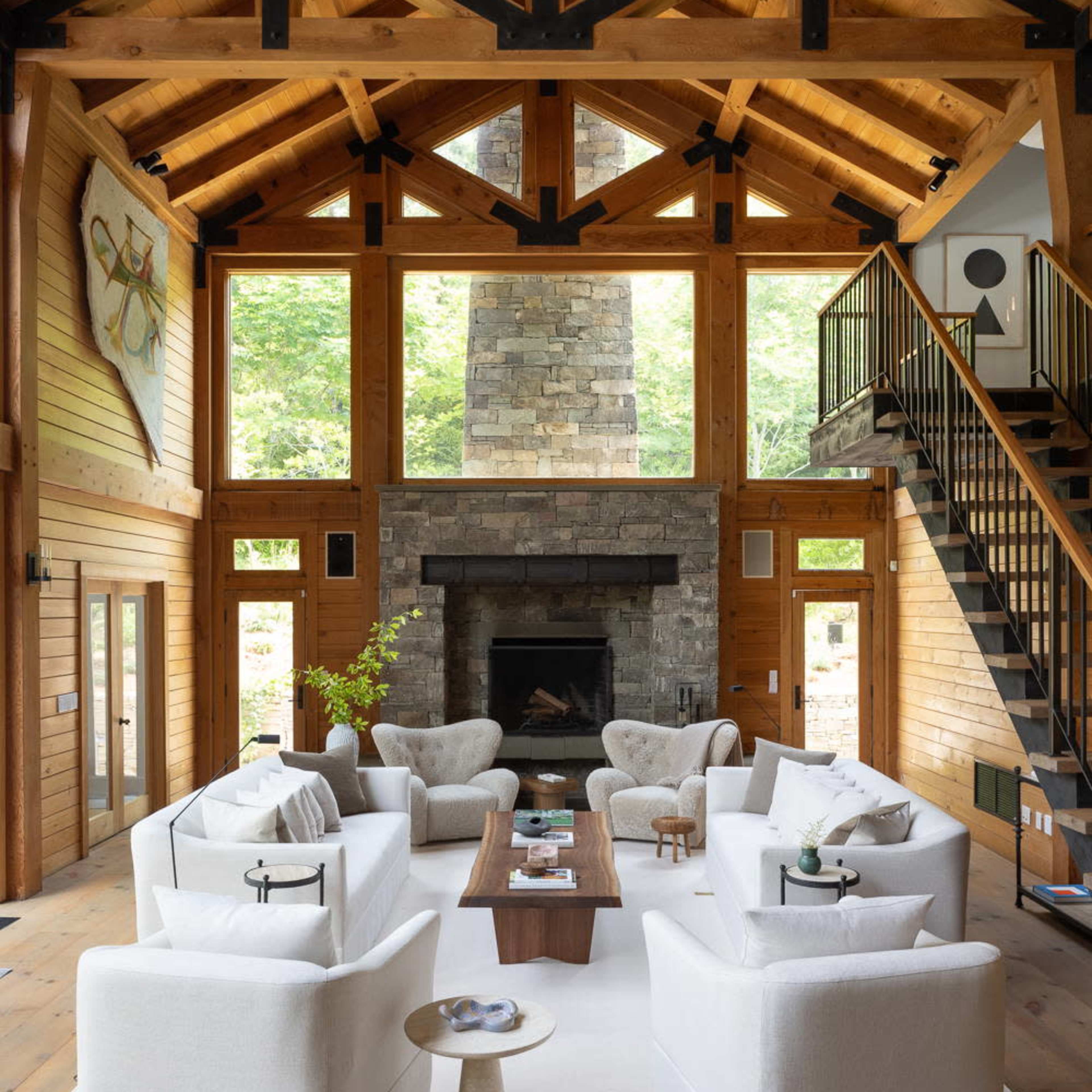 A spacious living room features vaulted wooden ceilings, a stone fireplace, and modern furniture arranged around a central coffee table.