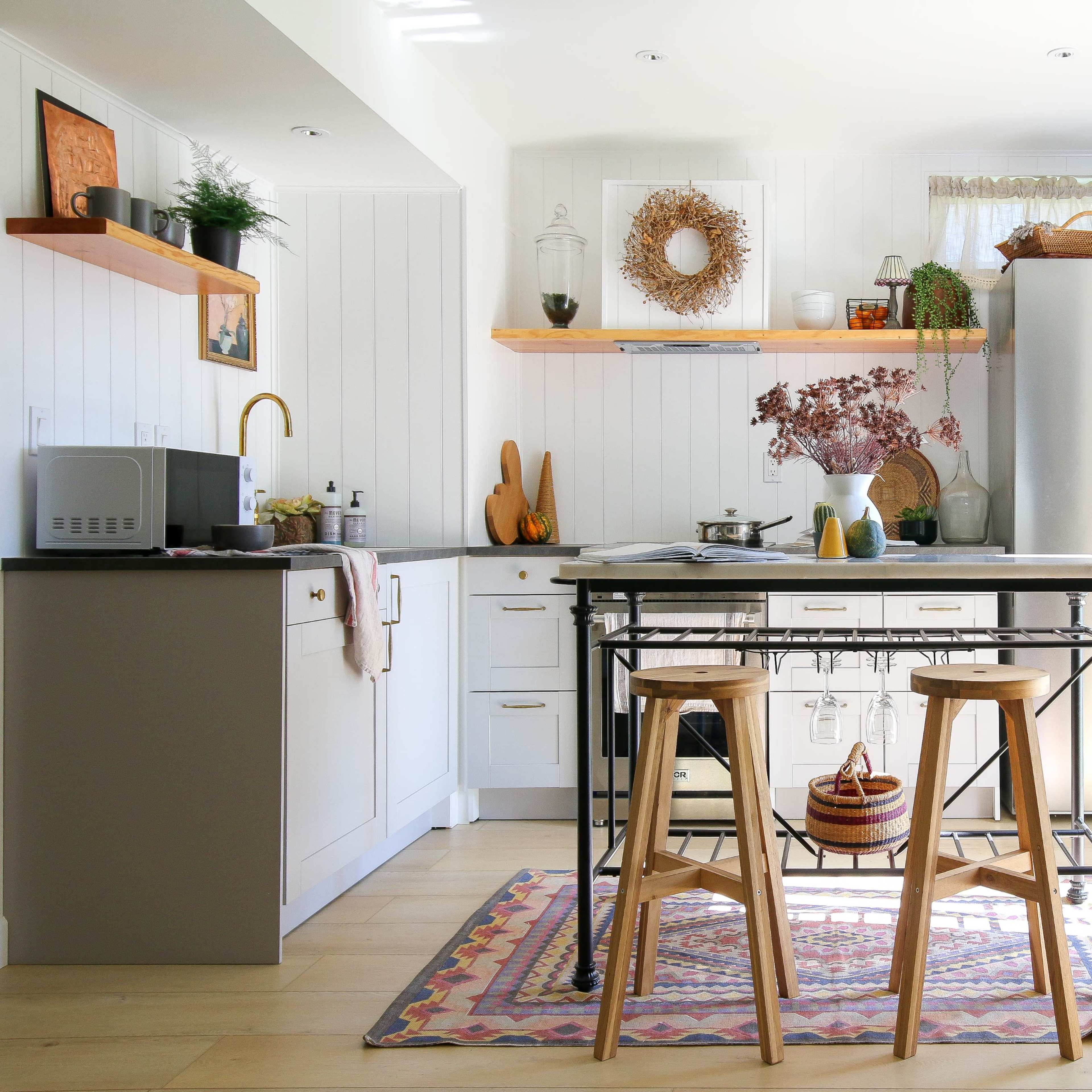 A modern kitchen features a central island with two wooden stools, surrounded by light-colored cabinetry, stainless steel appliances, and decorative elements.