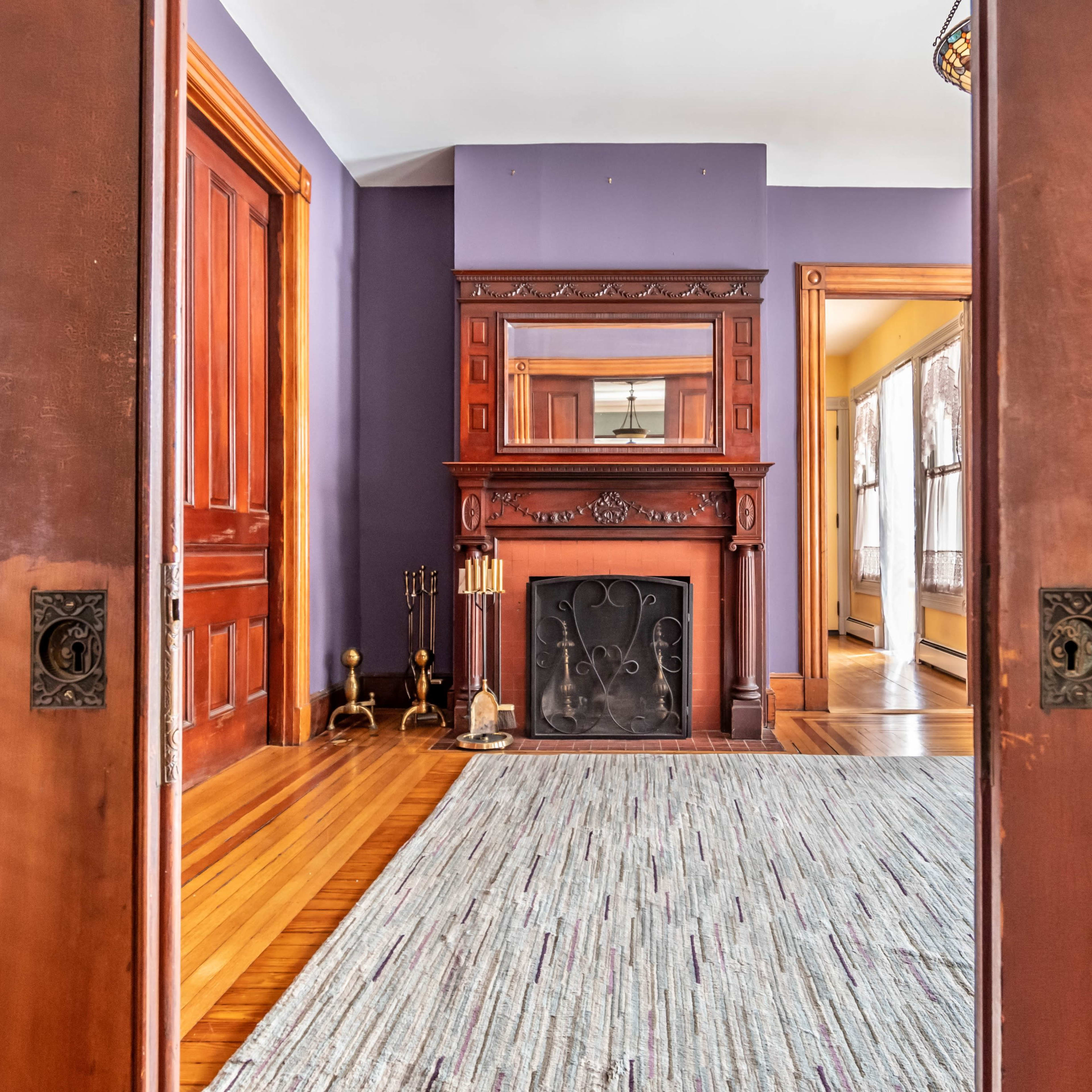 A view through open wooden doors reveals a room with a fireplace and a patterned rug on a wooden floor.