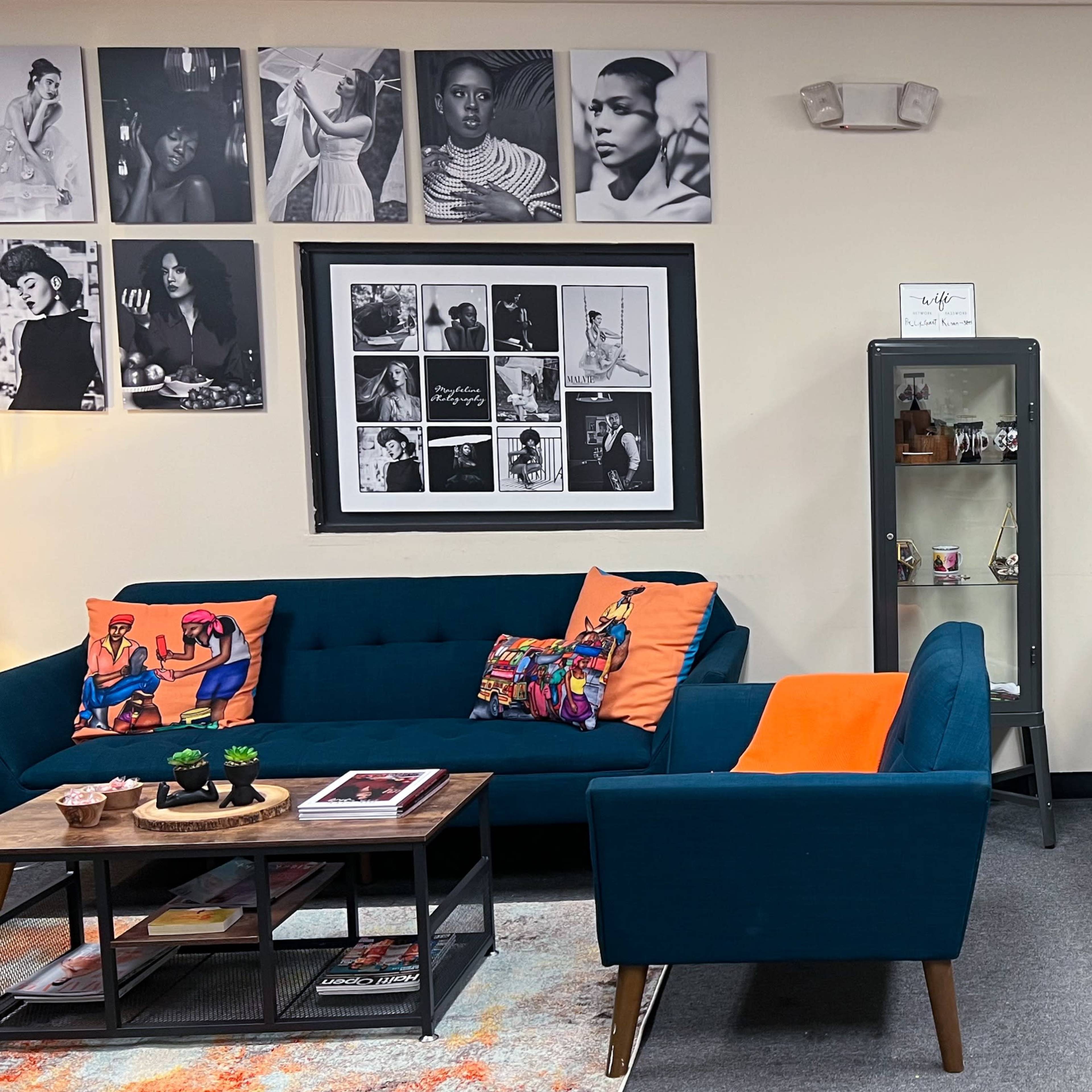 A neatly arranged office reception area with a blue sofa, an orange accent chair, a coffee table, and black-and-white photos on the walls.