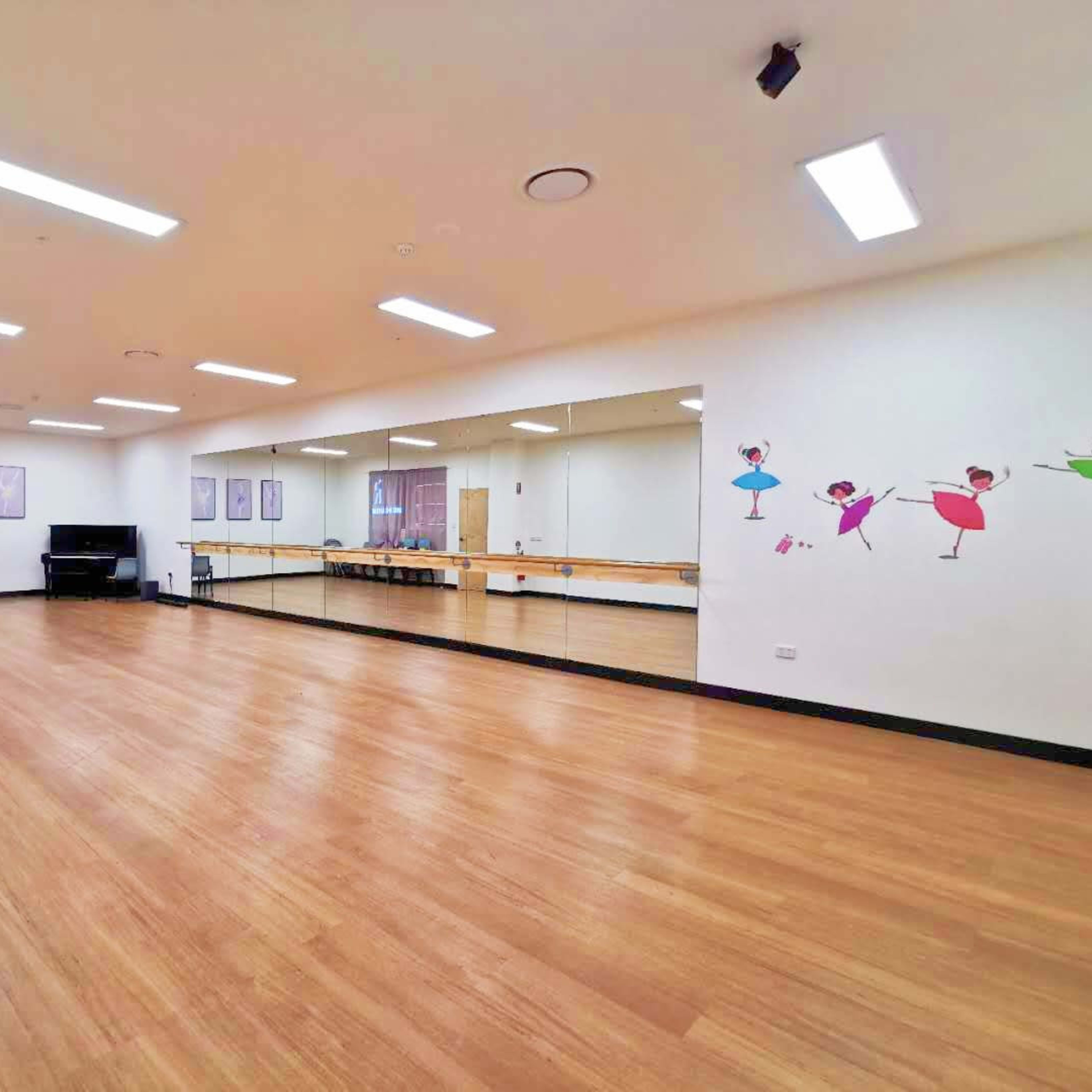 A spacious dance studio with wooden flooring, mirrors on one wall, and colorful ballet-themed decorations.