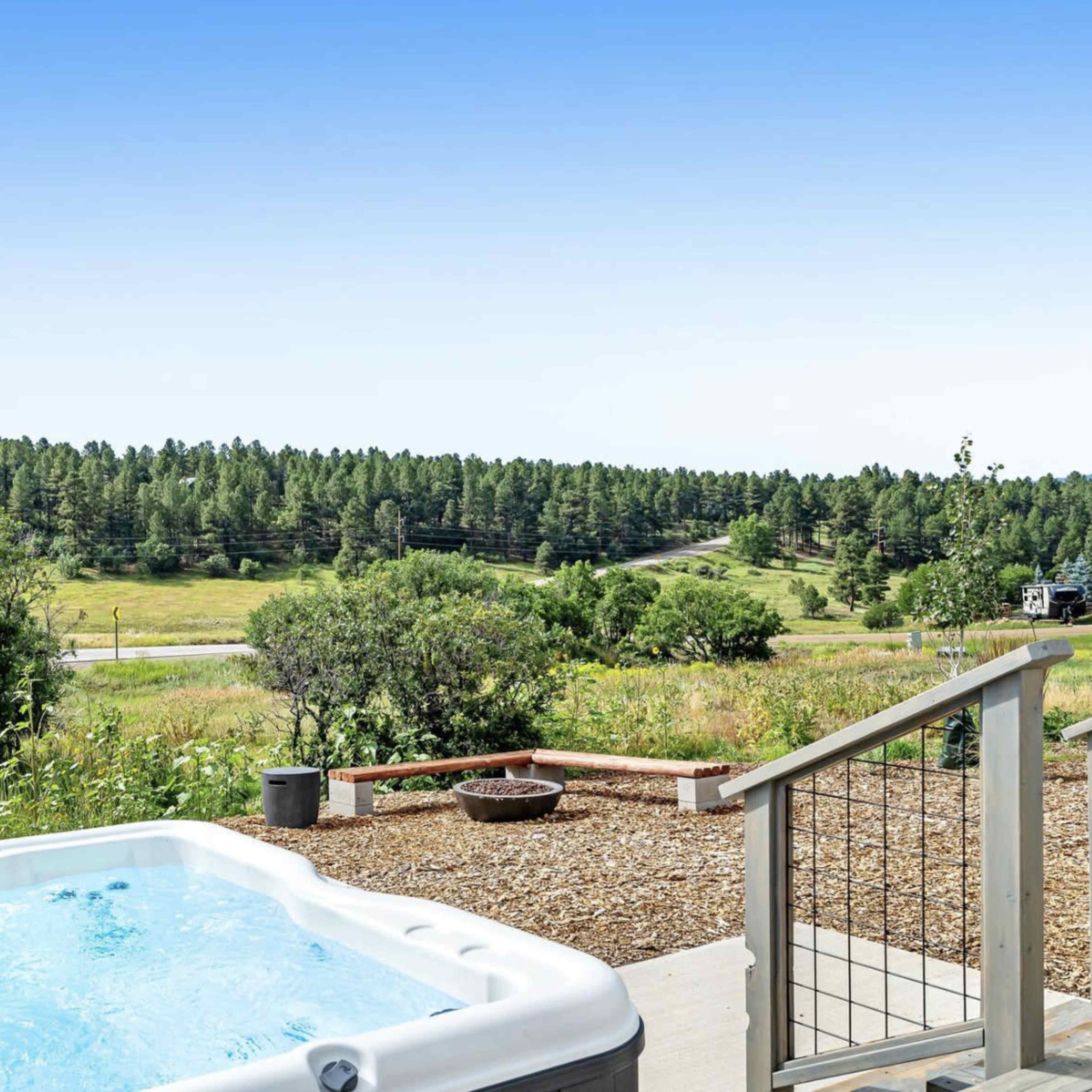 A hot tub is situated on a patio overlooking a green landscape with trees and a road in the background.