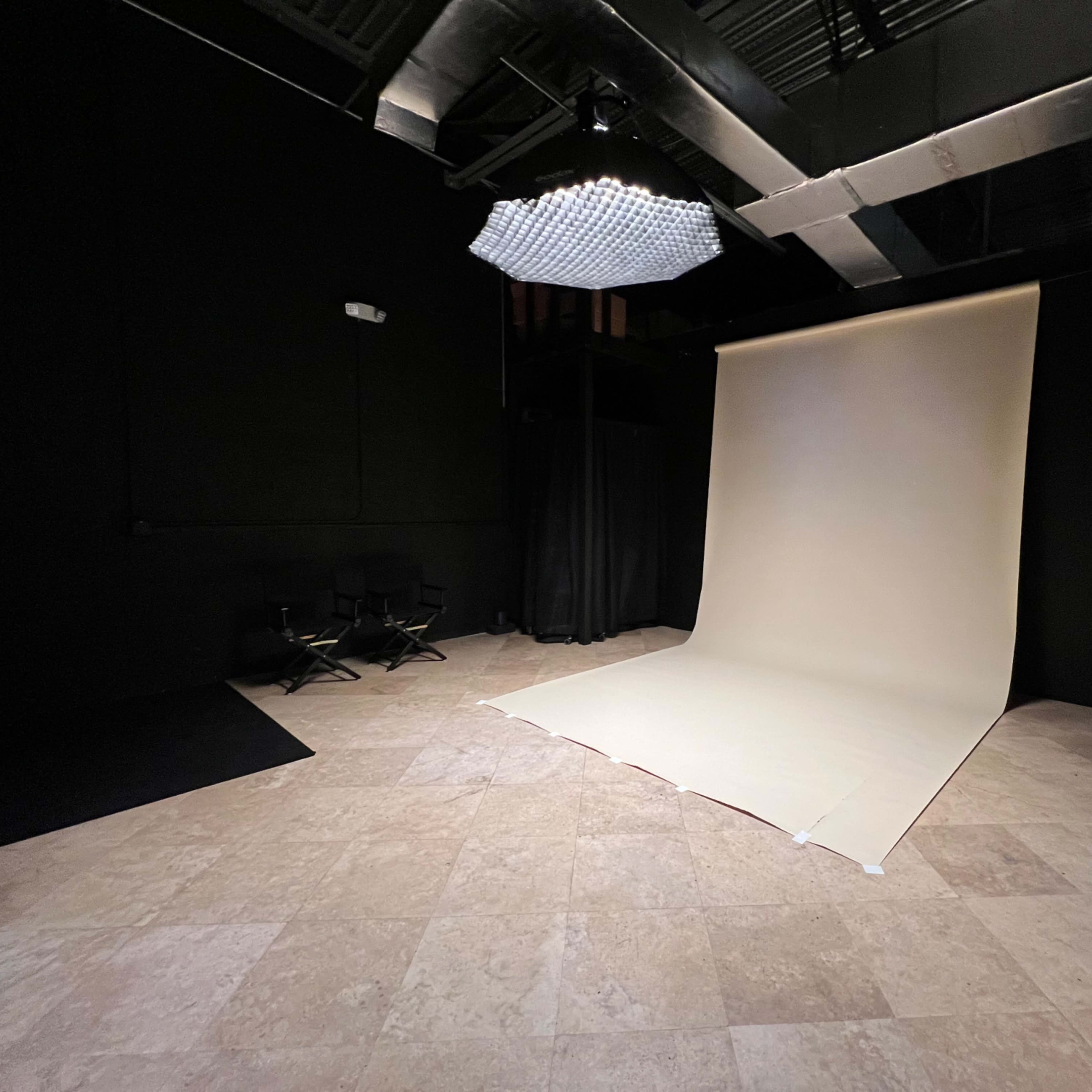 A photography studio with a light-colored backdrop, black walls, and a spotlight above.