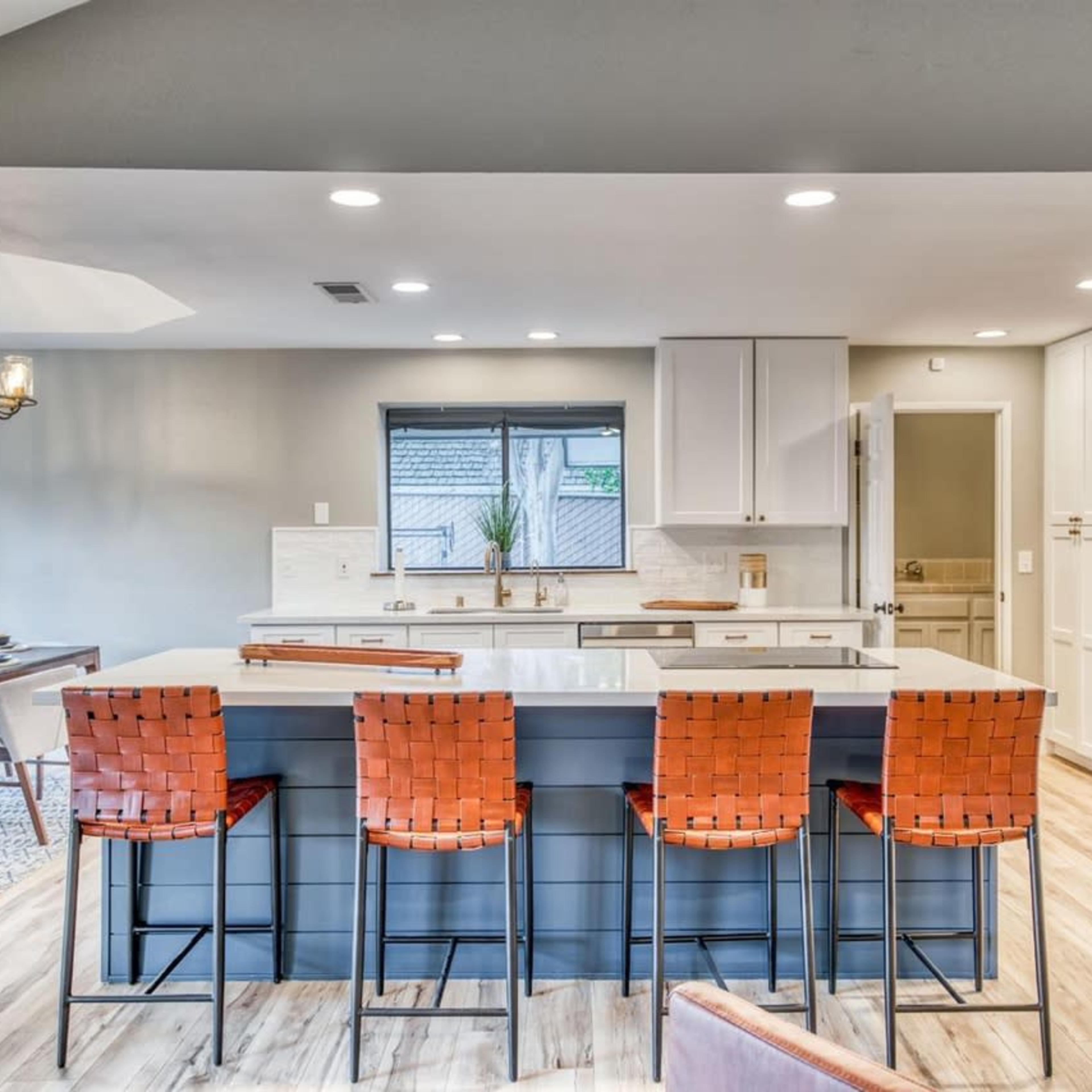 A modern kitchen with a large island, four bar stools, and an adjacent dining area.