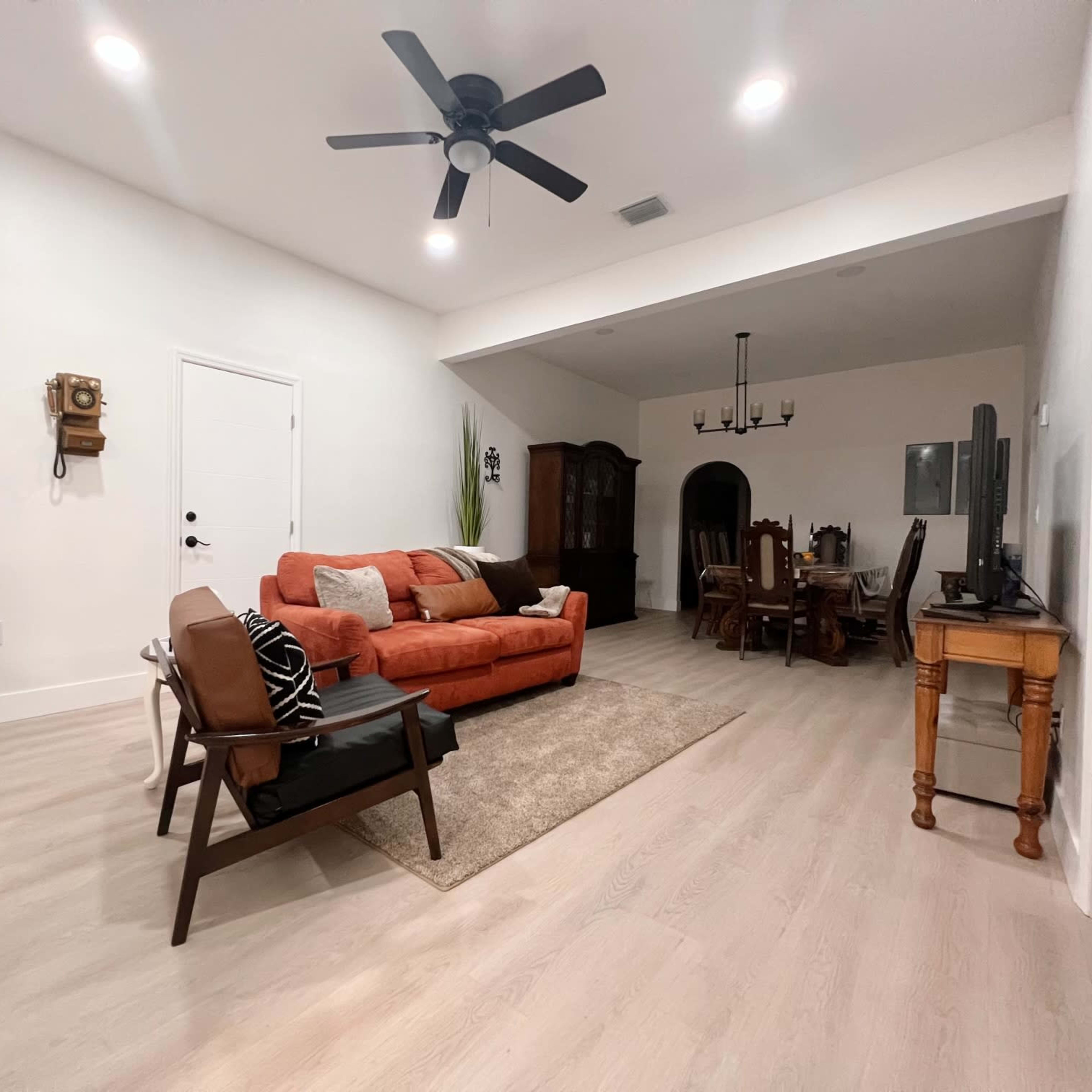 The living area features an orange sofa, a wooden coffee table, a glass cabinet, and a dining area with a dark wooden table and chairs.