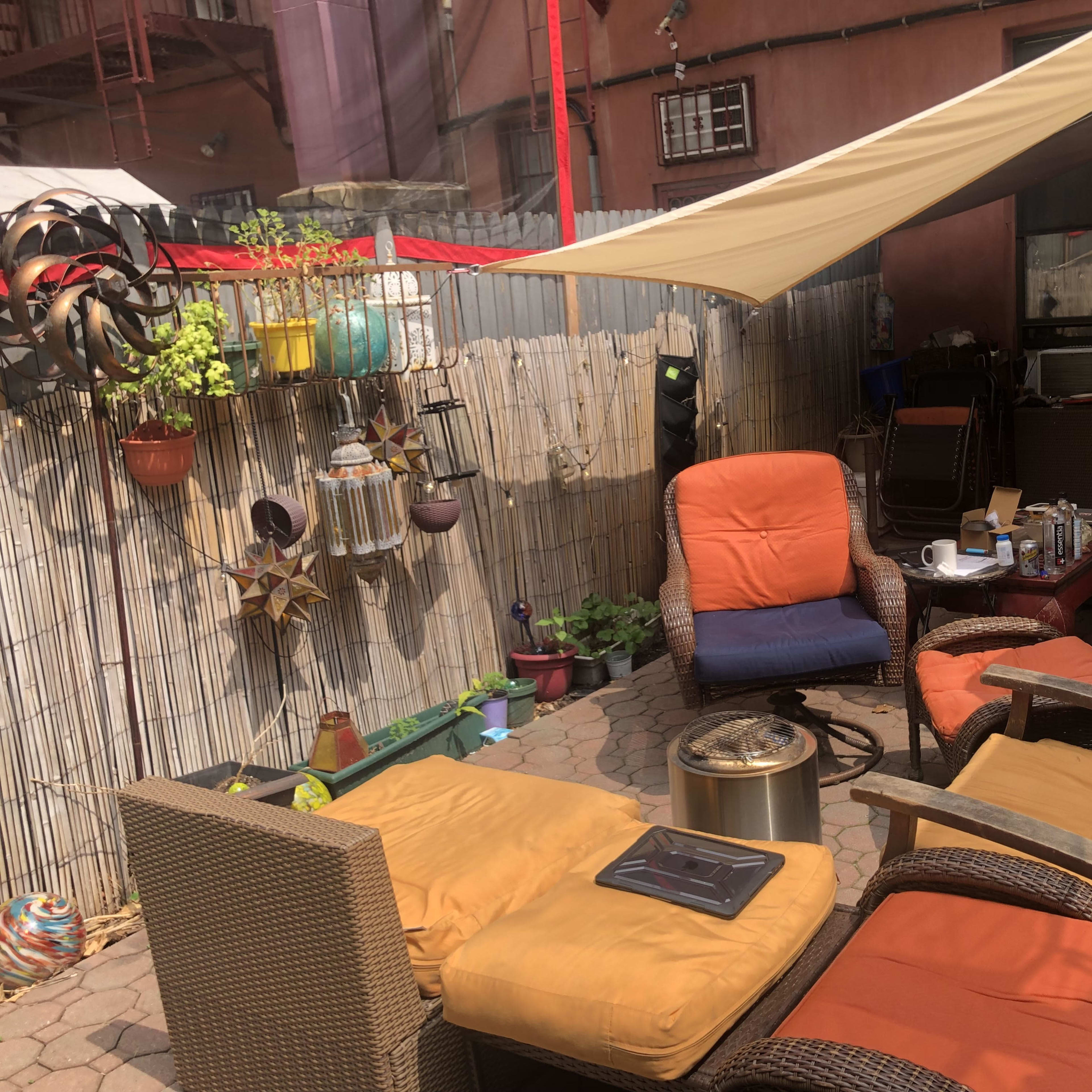 A backyard patio area with wicker furniture, a fire pit, and various plants and decorations.