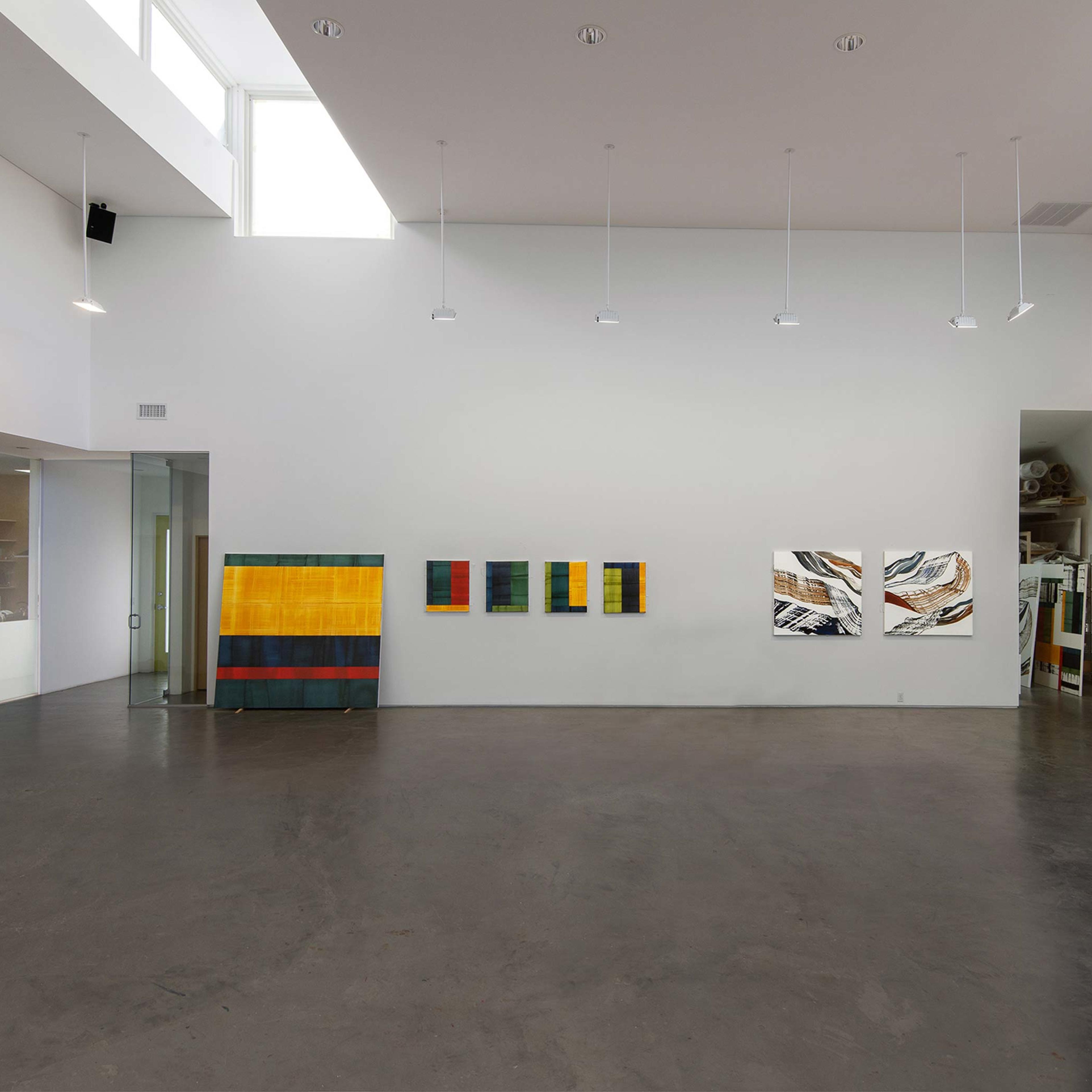 A modern art gallery with high ceilings, featuring abstract paintings on the walls and a polished concrete floor.