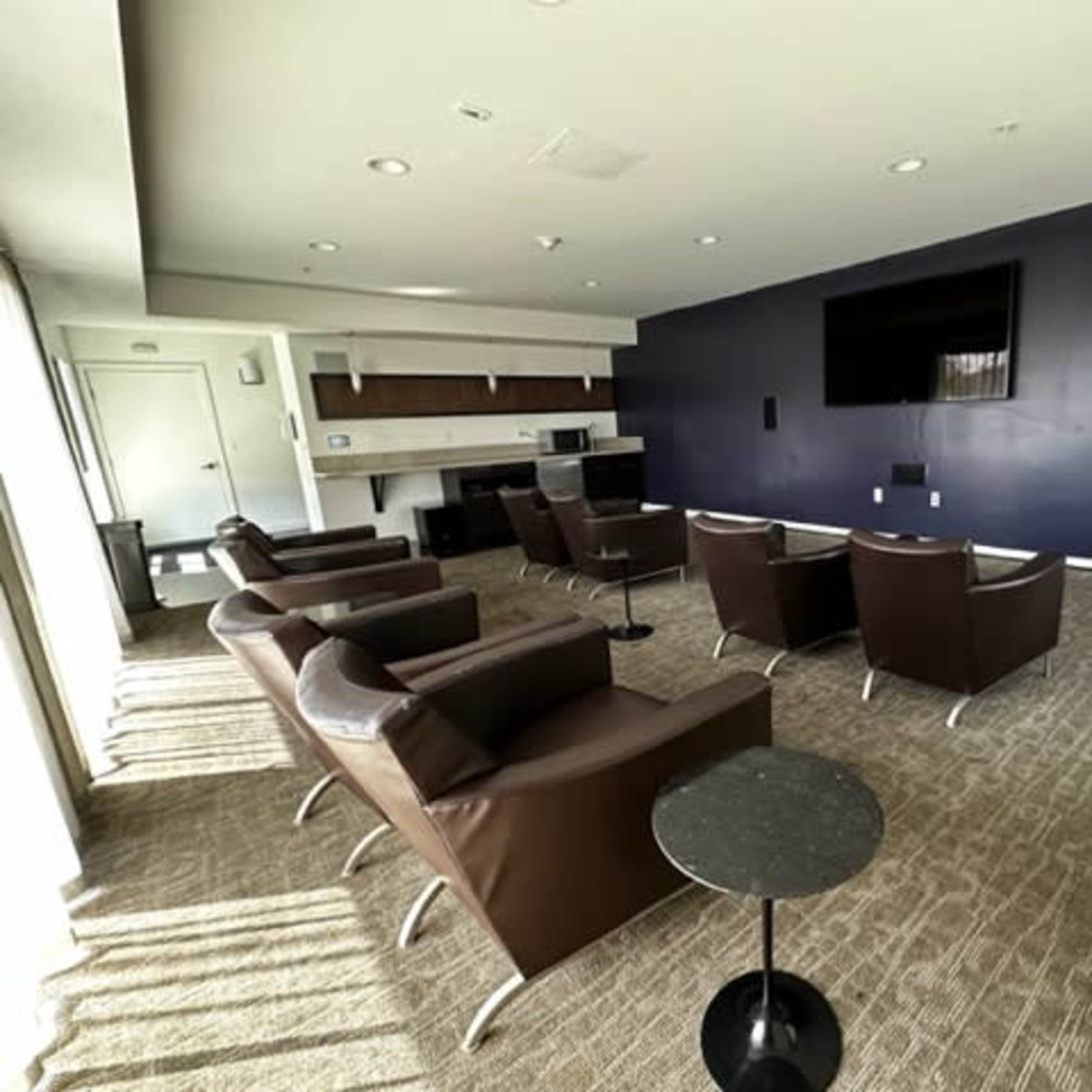 A spacious lounge area with several brown leather chairs arranged in front of a wall-mounted television and a small side table.