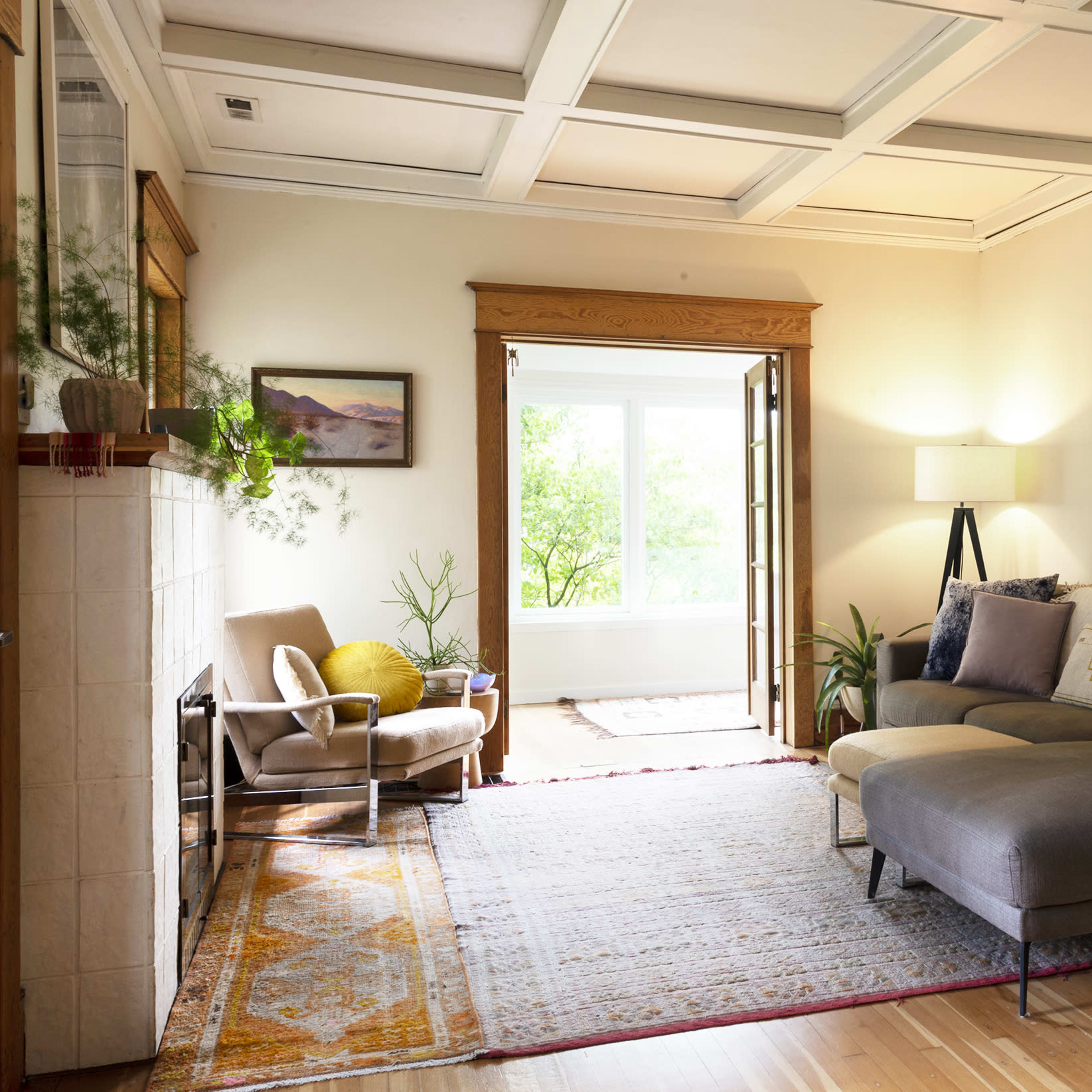 A cozy living room features a sectional sofa, plants, and large windows that invite natural light.