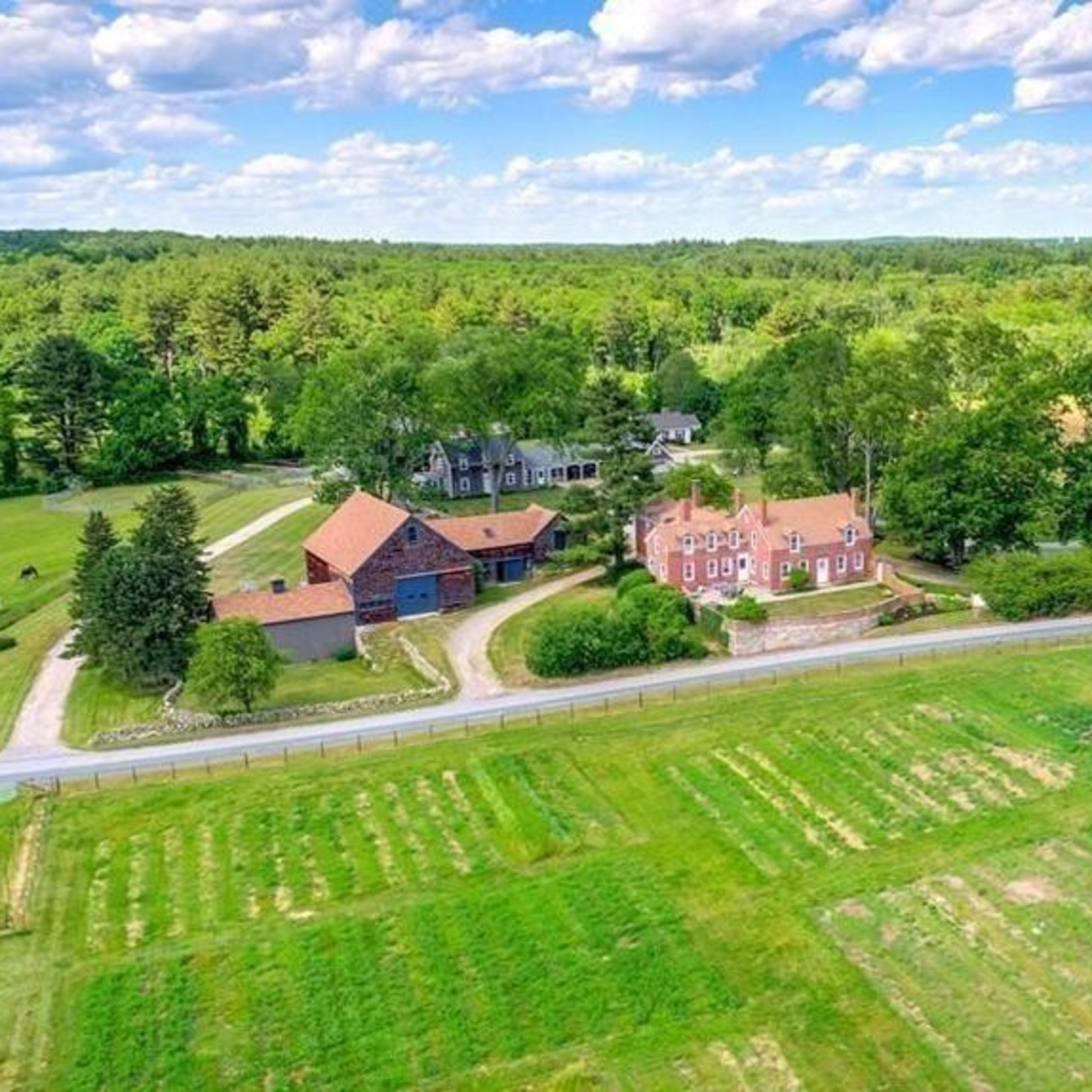 An aerial view of a rural property featuring multiple buildings, green fields, and a winding road surrounded by trees.