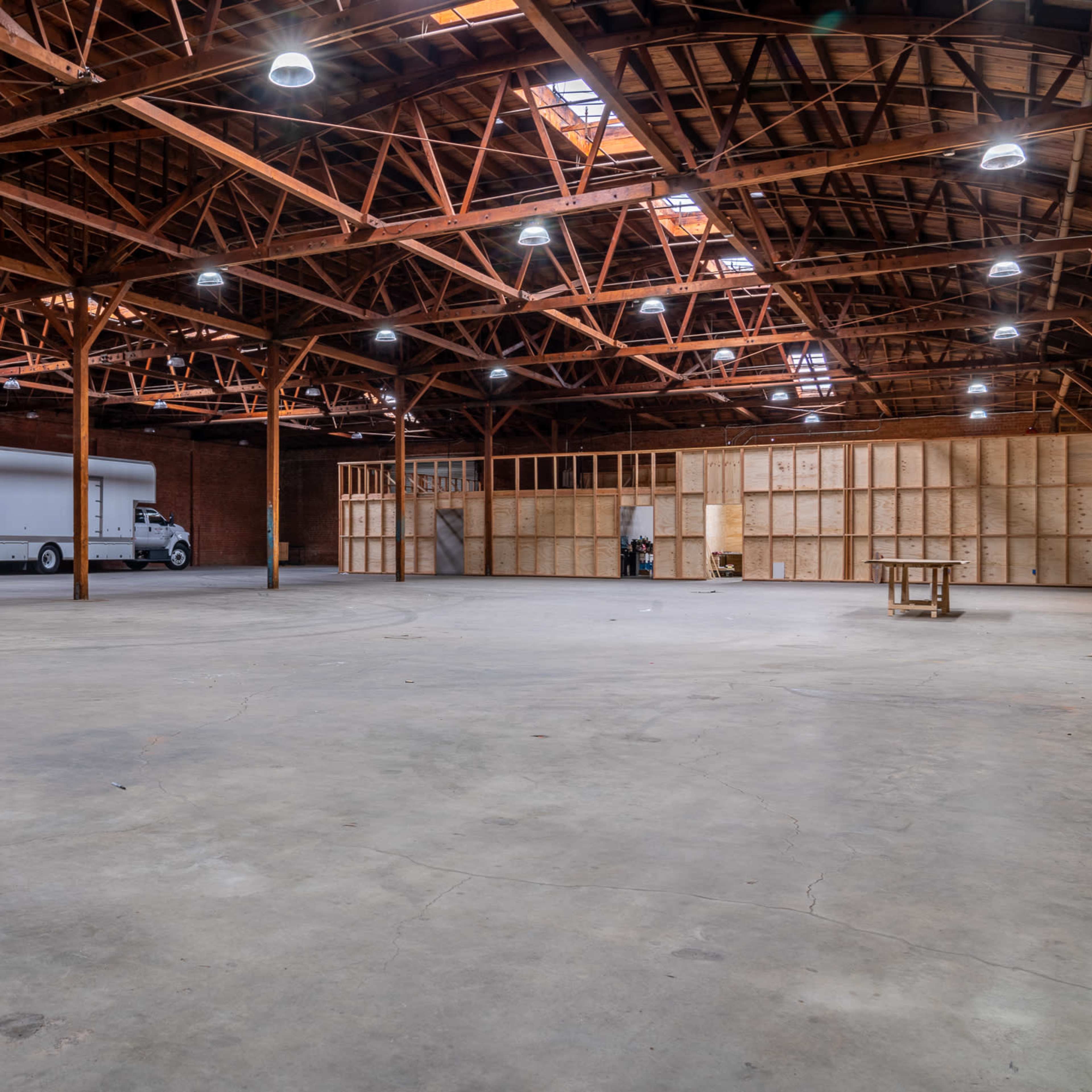 A spacious, empty warehouse with exposed wooden beams and a large truck parked near a partitioned area.