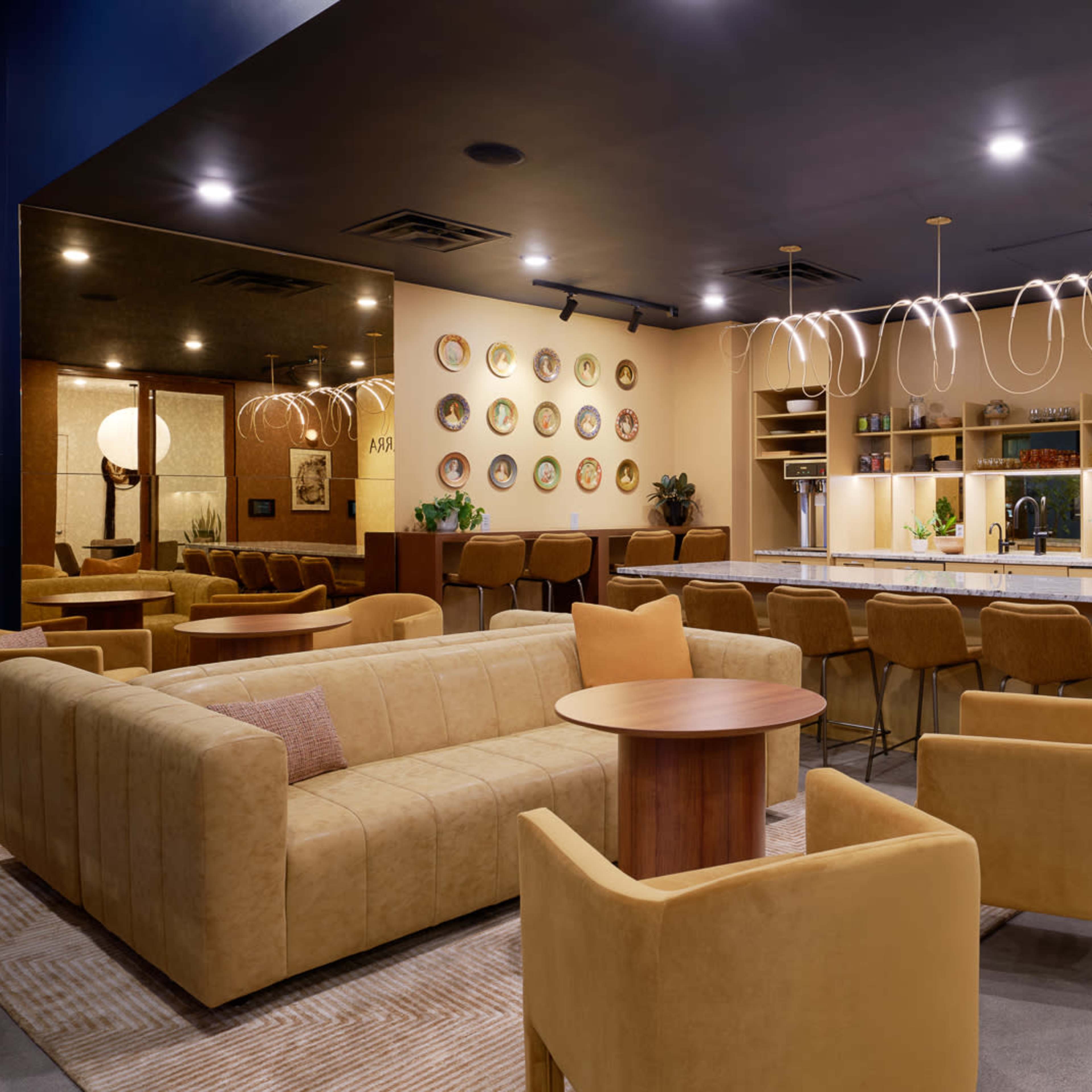 A modern lounge area with a yellow color scheme, featuring a large beige sofa, matching chairs, and a bar with decorative plates on the wall.