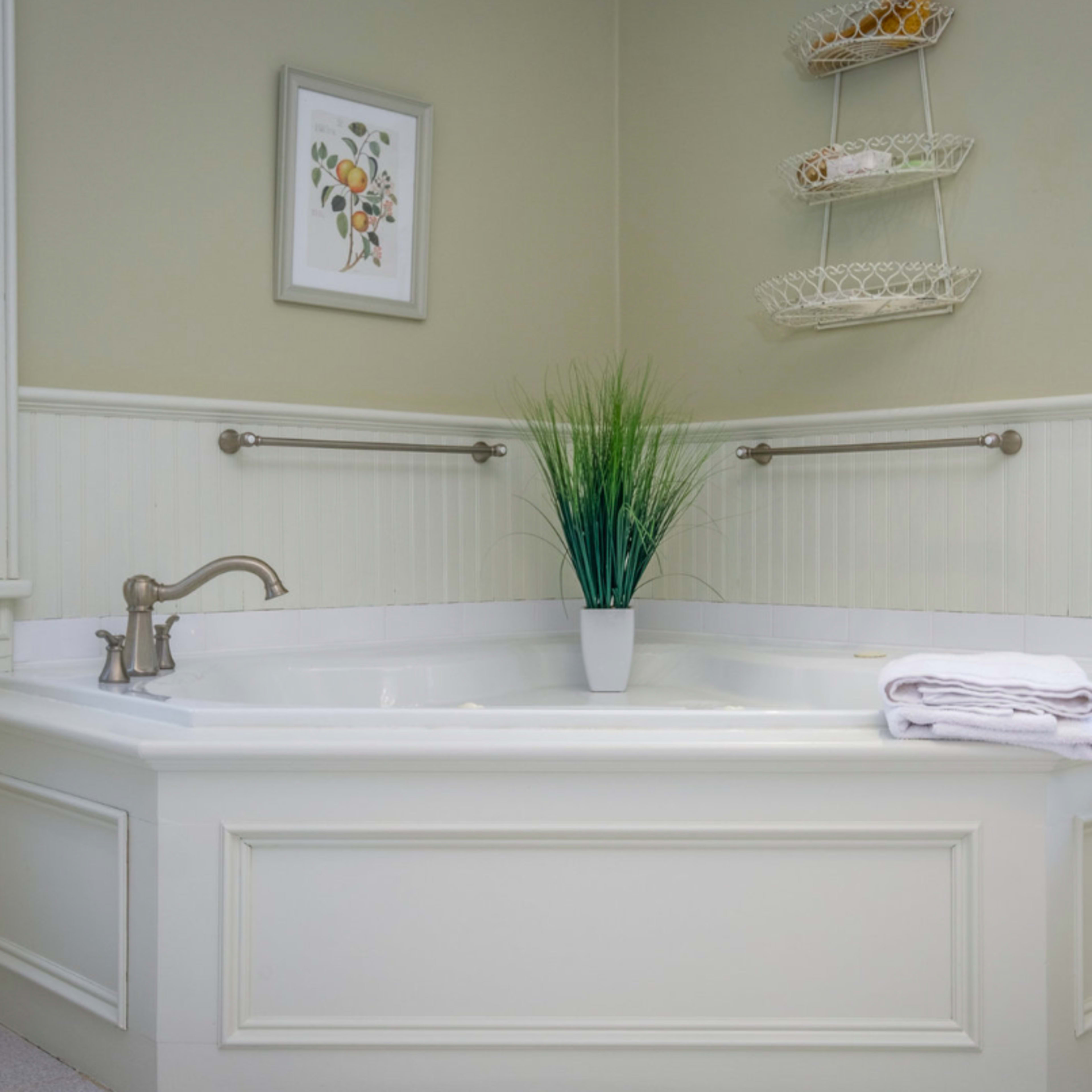 A corner bathtub with a potted plant and neatly folded towels on a ledge in a well-lit bathroom.