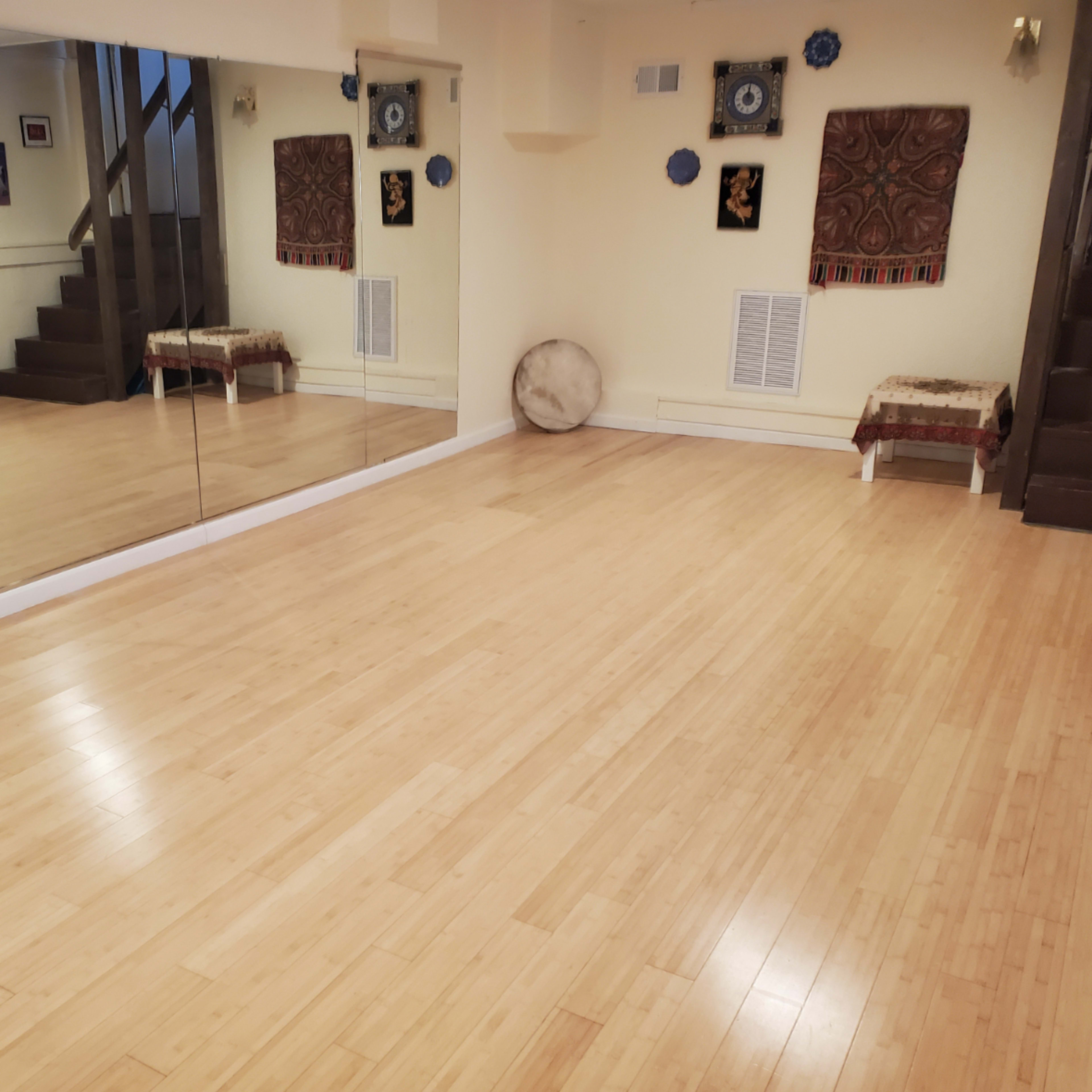 A spacious room with bamboo flooring, a large mirror on one wall, and decorative wall hangings.