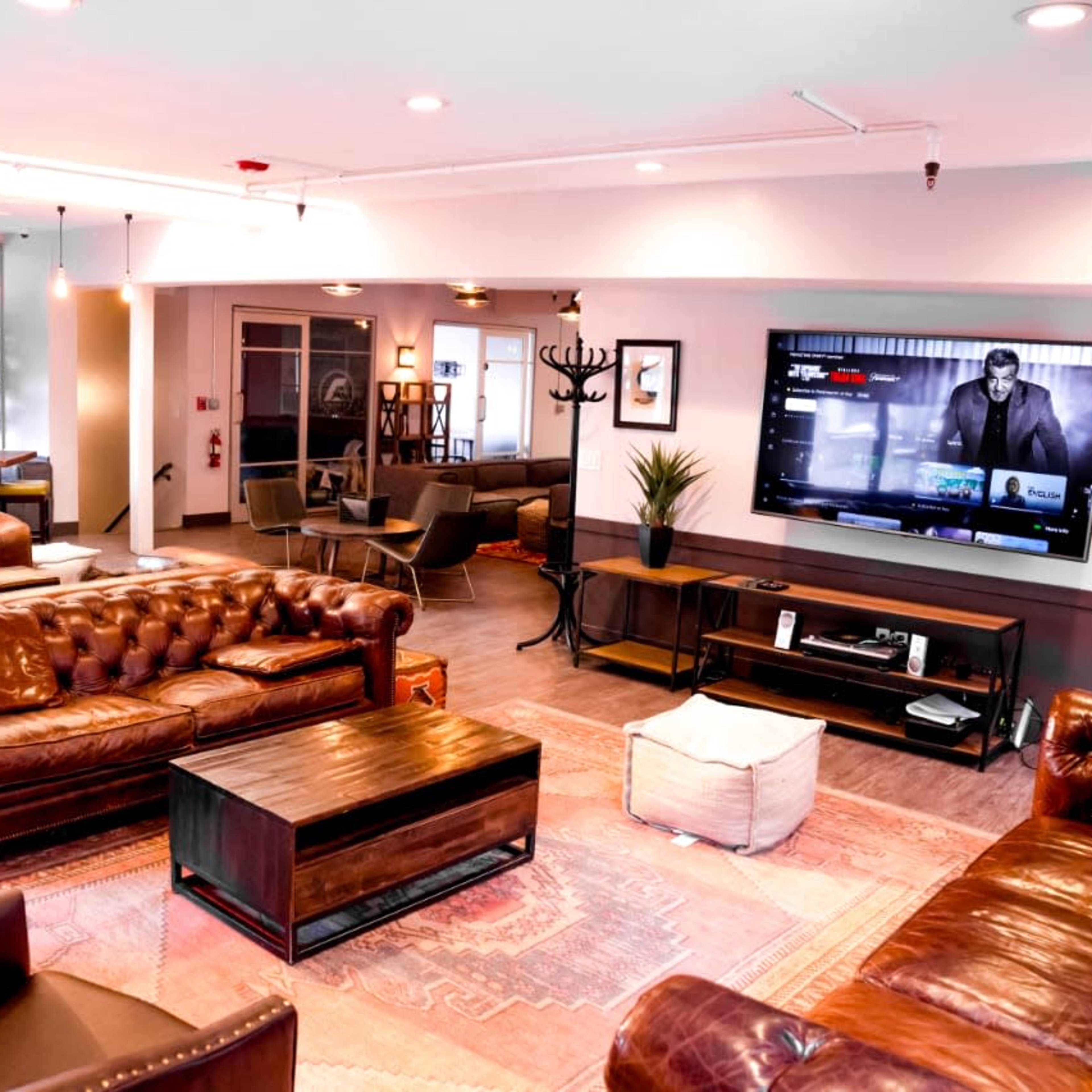 A modern lounge area featuring leather sofas, a coffee table, and a large TV mounted on the wall.