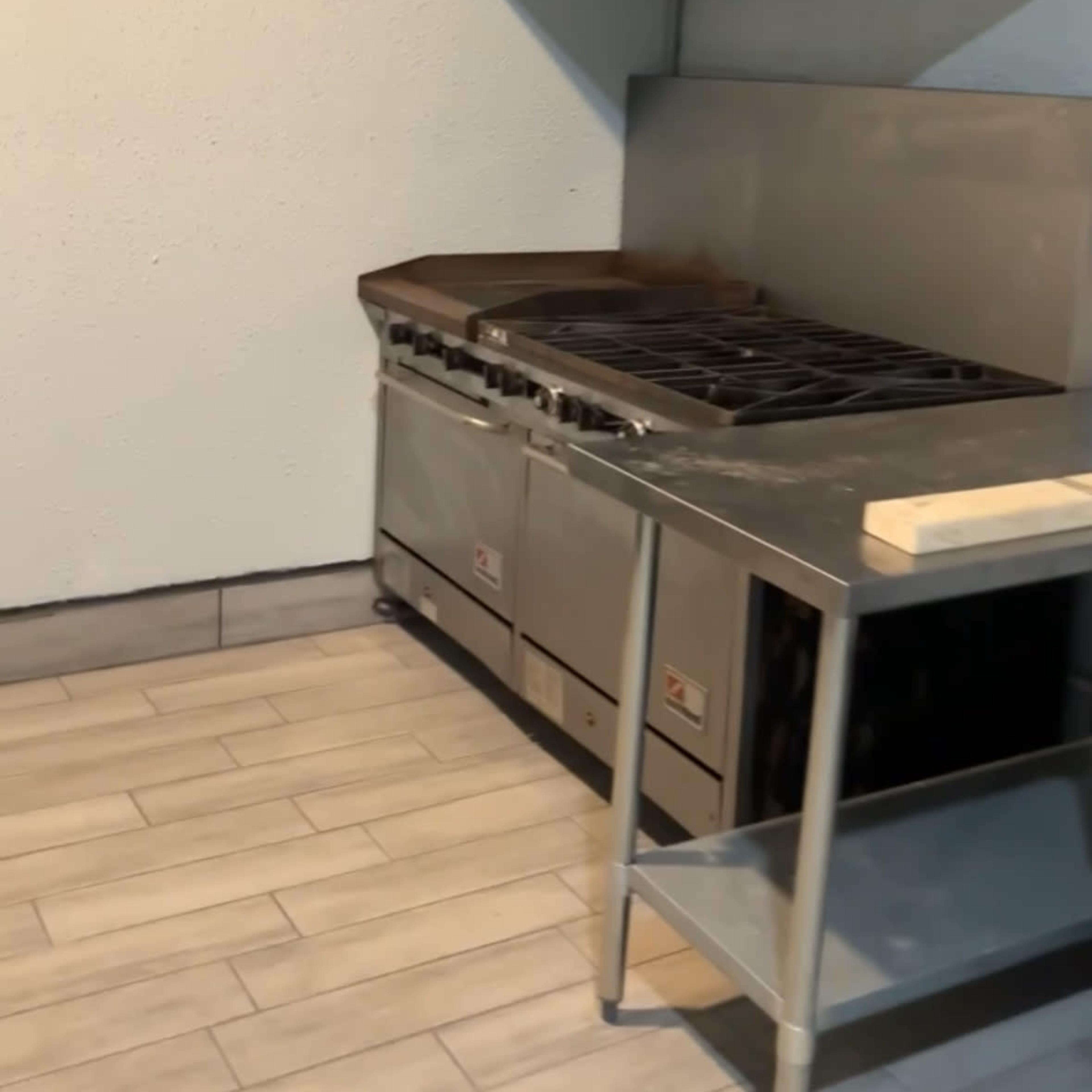A commercial kitchen space featuring a stainless steel cooking range with a ventilation hood and a metal table beside it.