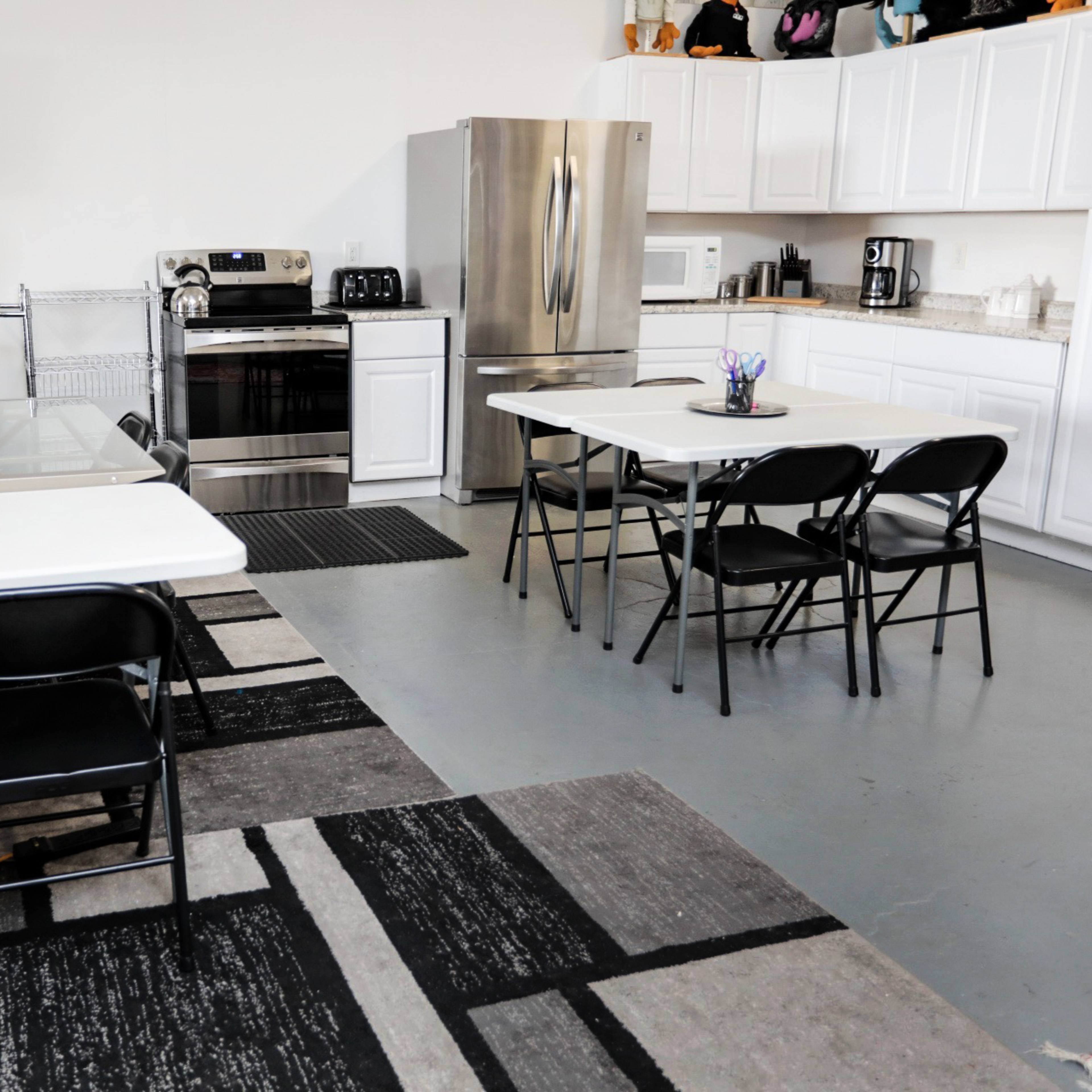 A functional kitchen and dining area featuring a large stainless steel fridge, an oven, white cabinets, a black couch, and several tables with chairs.